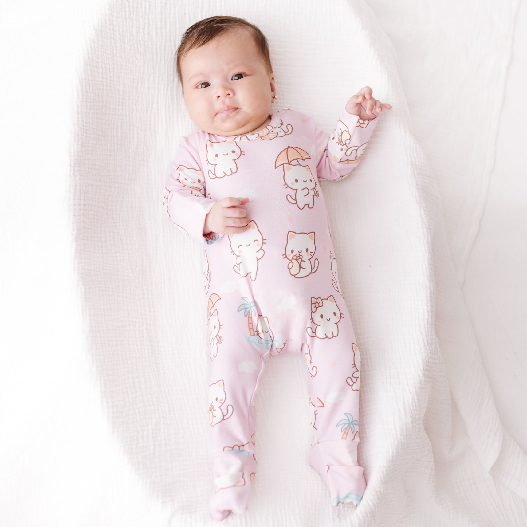 Baby wearing a pink onesie with cartoon characters on a white blanket