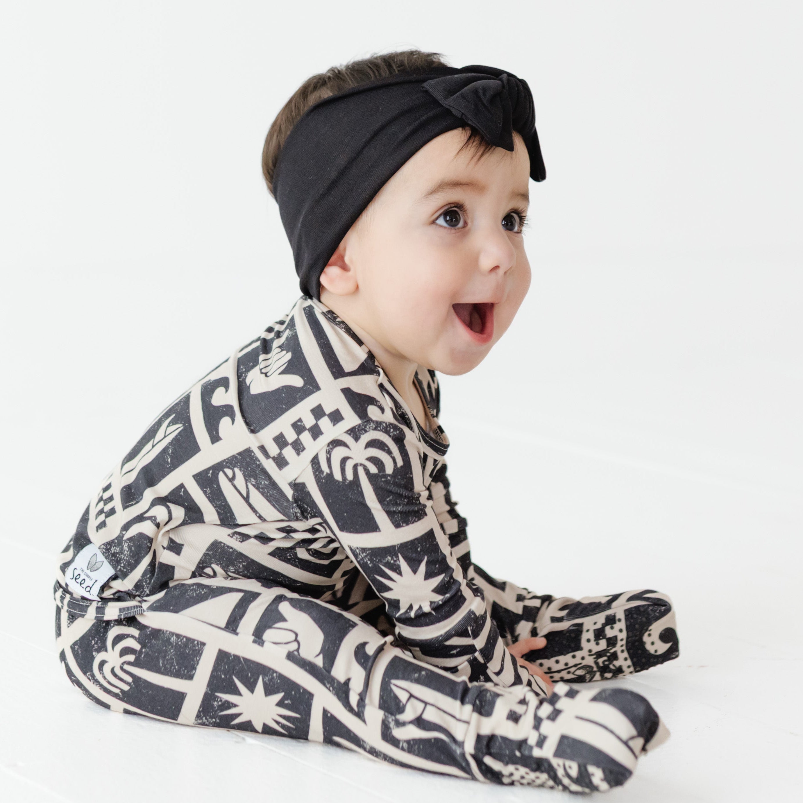 Baby wearing a patterned outfit and black headband on a white background
