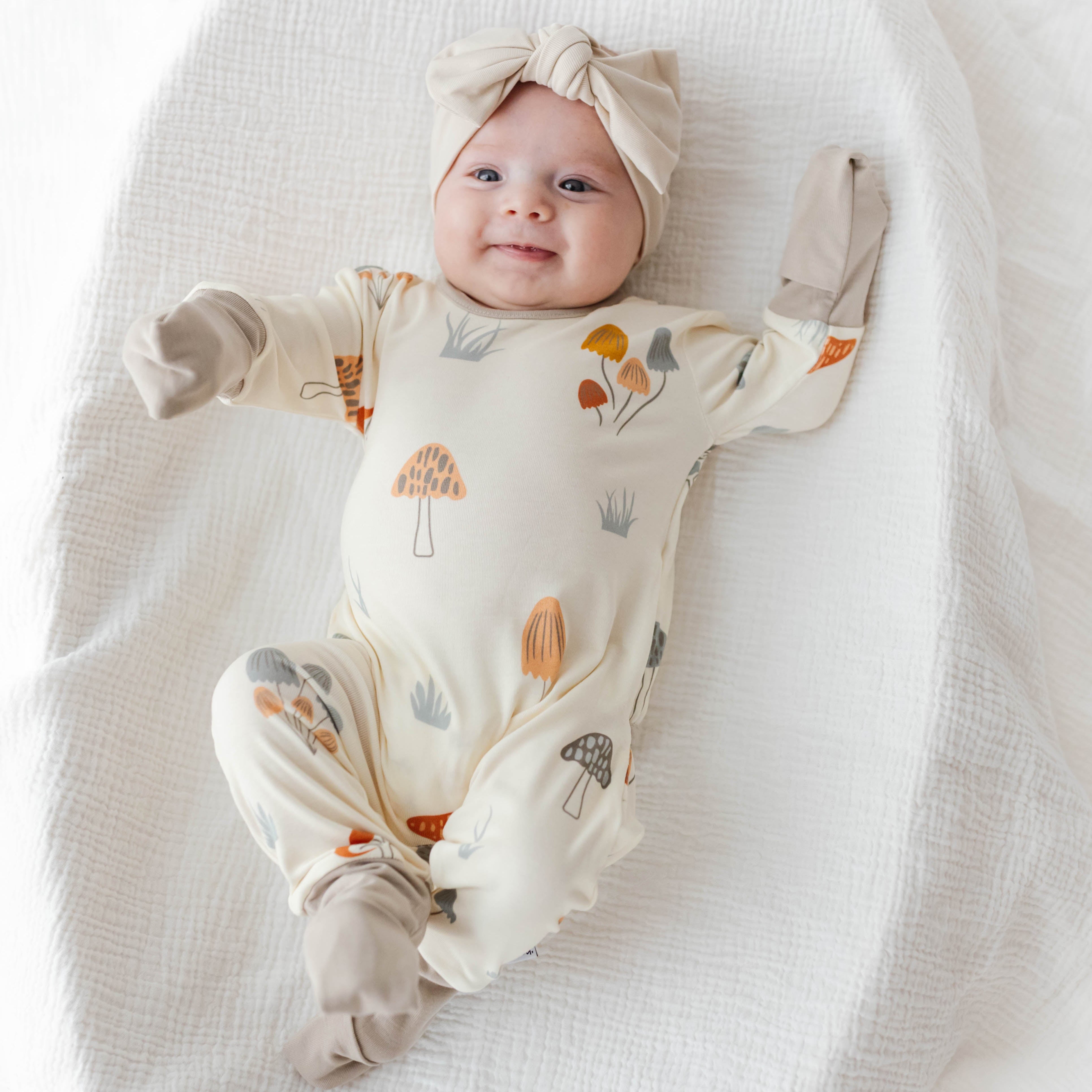Baby wearing a onesie with nature-themed prints on a white blanket