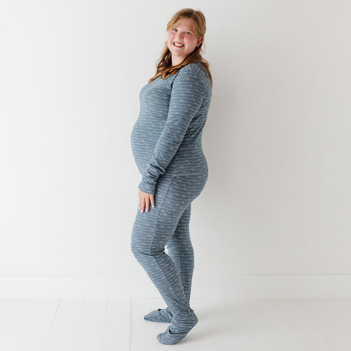 A smiling woman stands on white floor wearing blue romper with waves on it. 