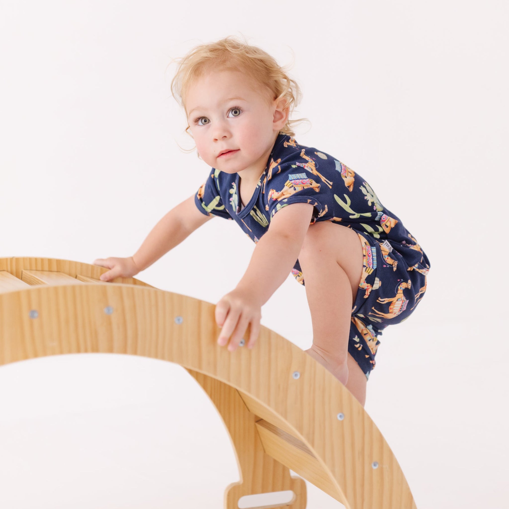 Child climbing on a wooden arch toy with a white background