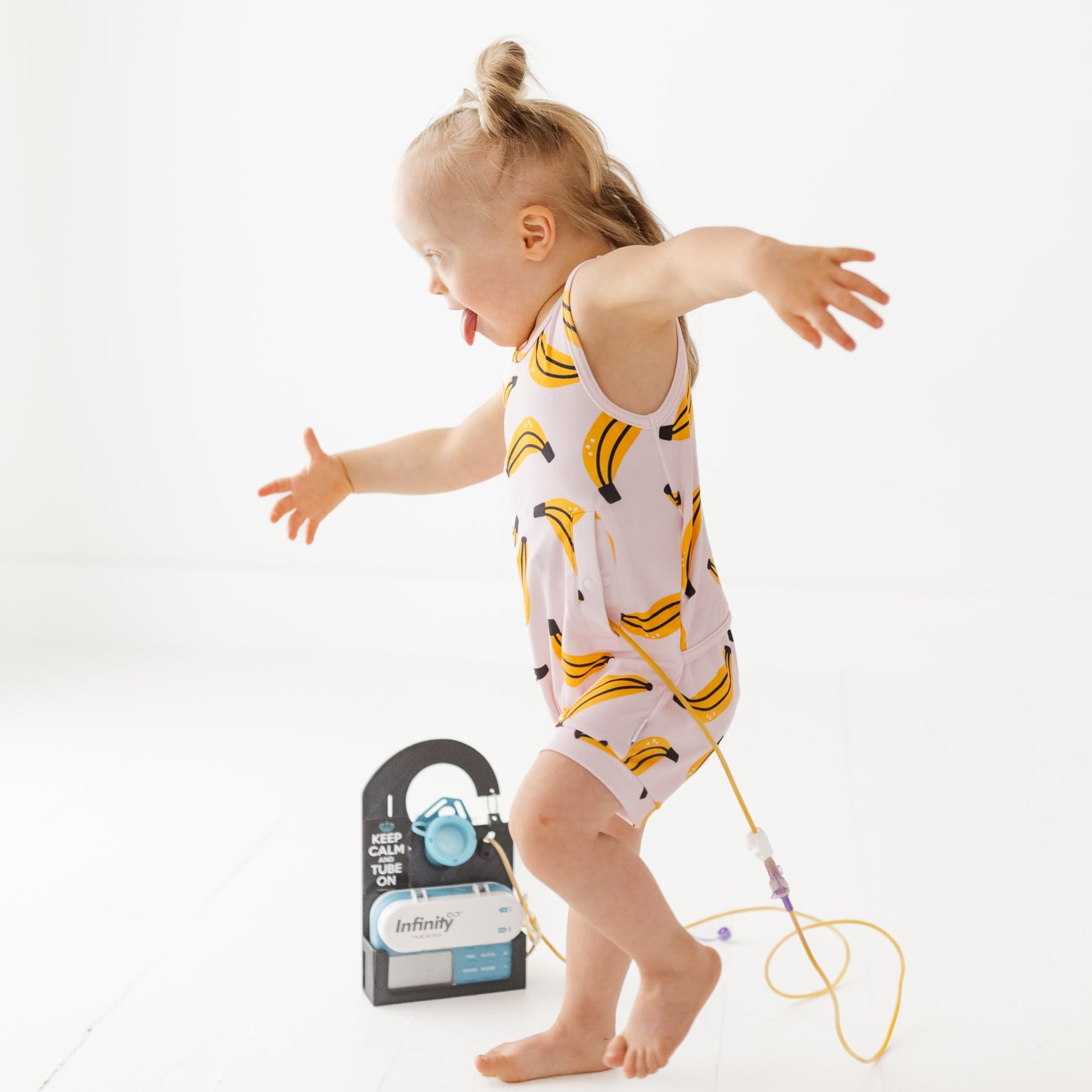 Child in a banana-patterned onesie with a gtube on a white background