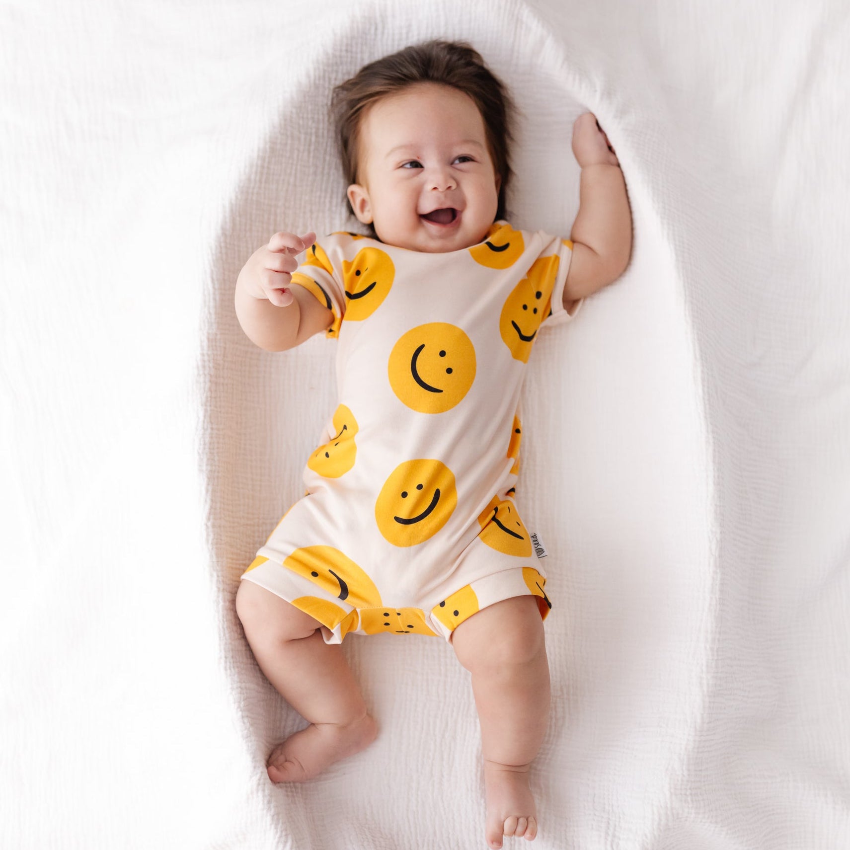 Baby wearing a yellow smiley face onesie on a white background