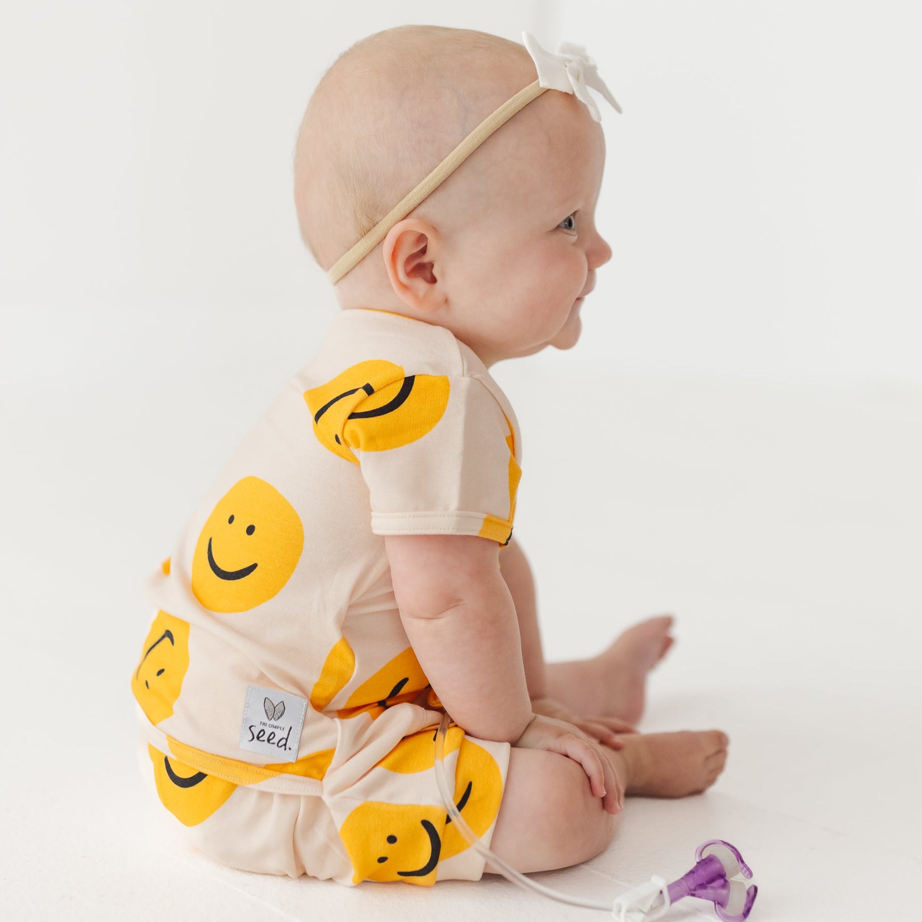 Baby wearing a white onesie with yellow smiley face patterns on a white background