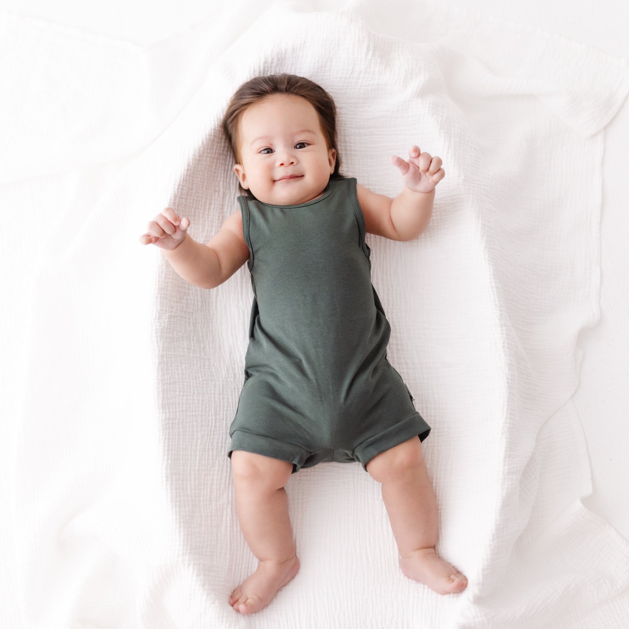 Baby wearing a green romper lying on a white blanket