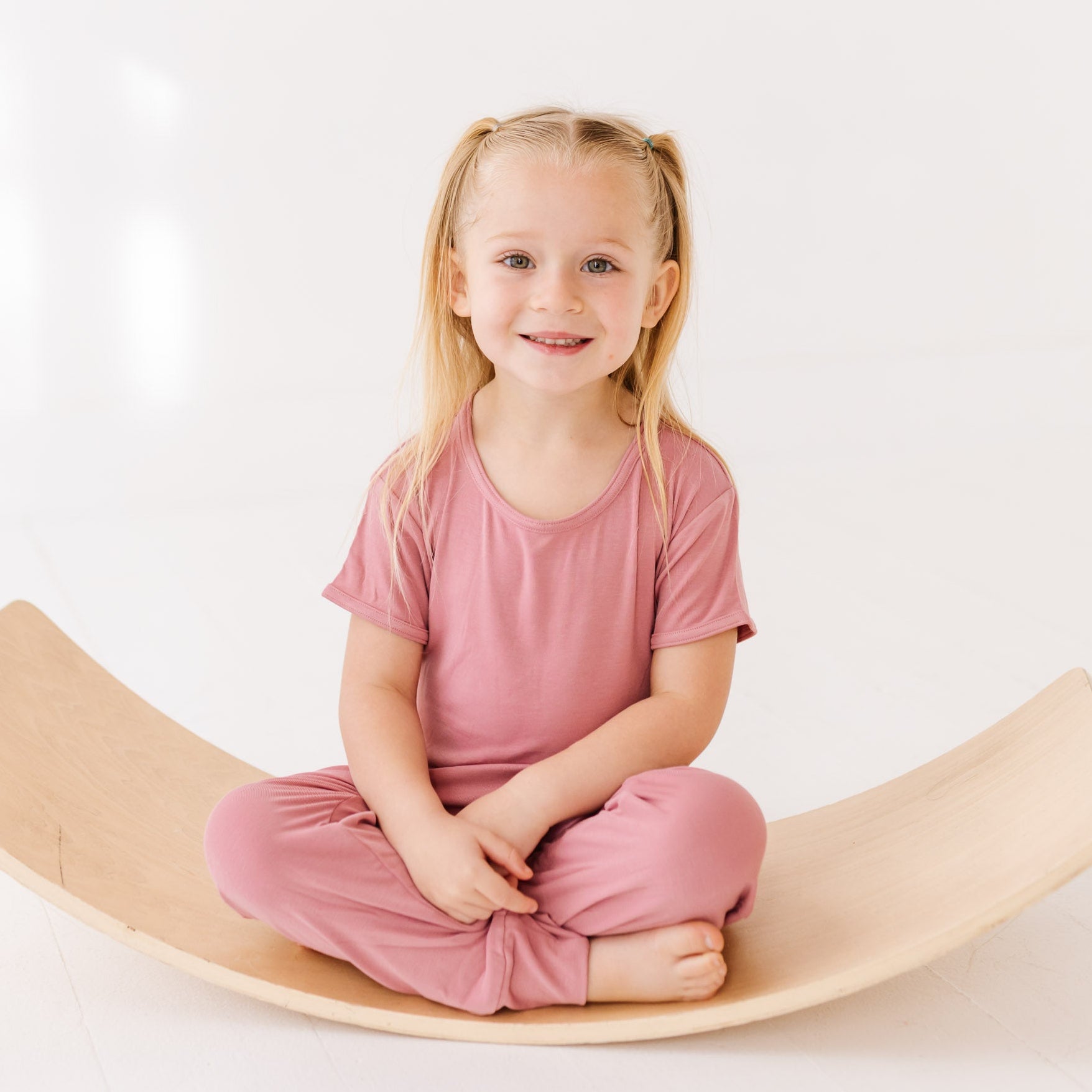 Young girl sitting on a wooden balance board against a white background