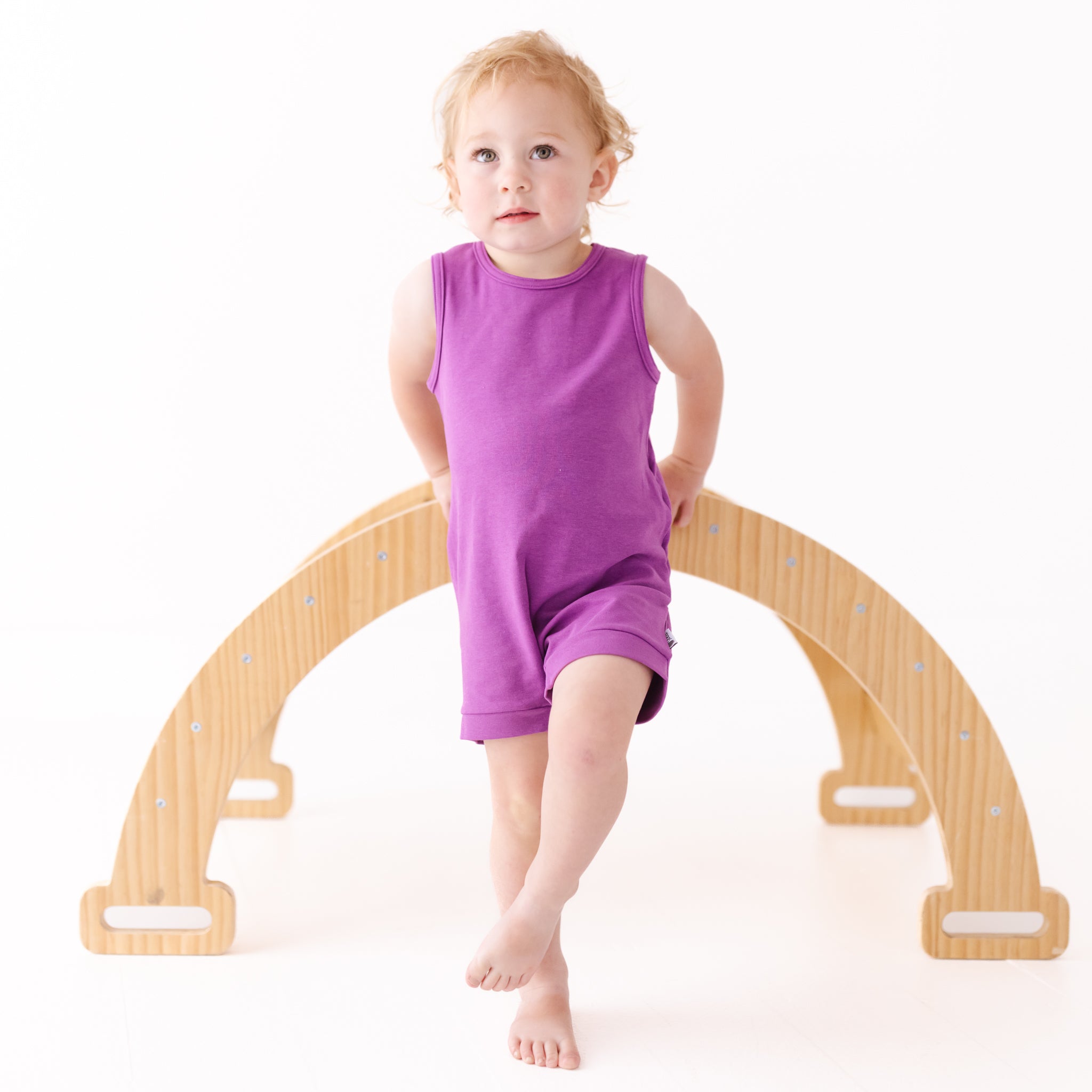 Child sitting on a wooden arch toy with a white background