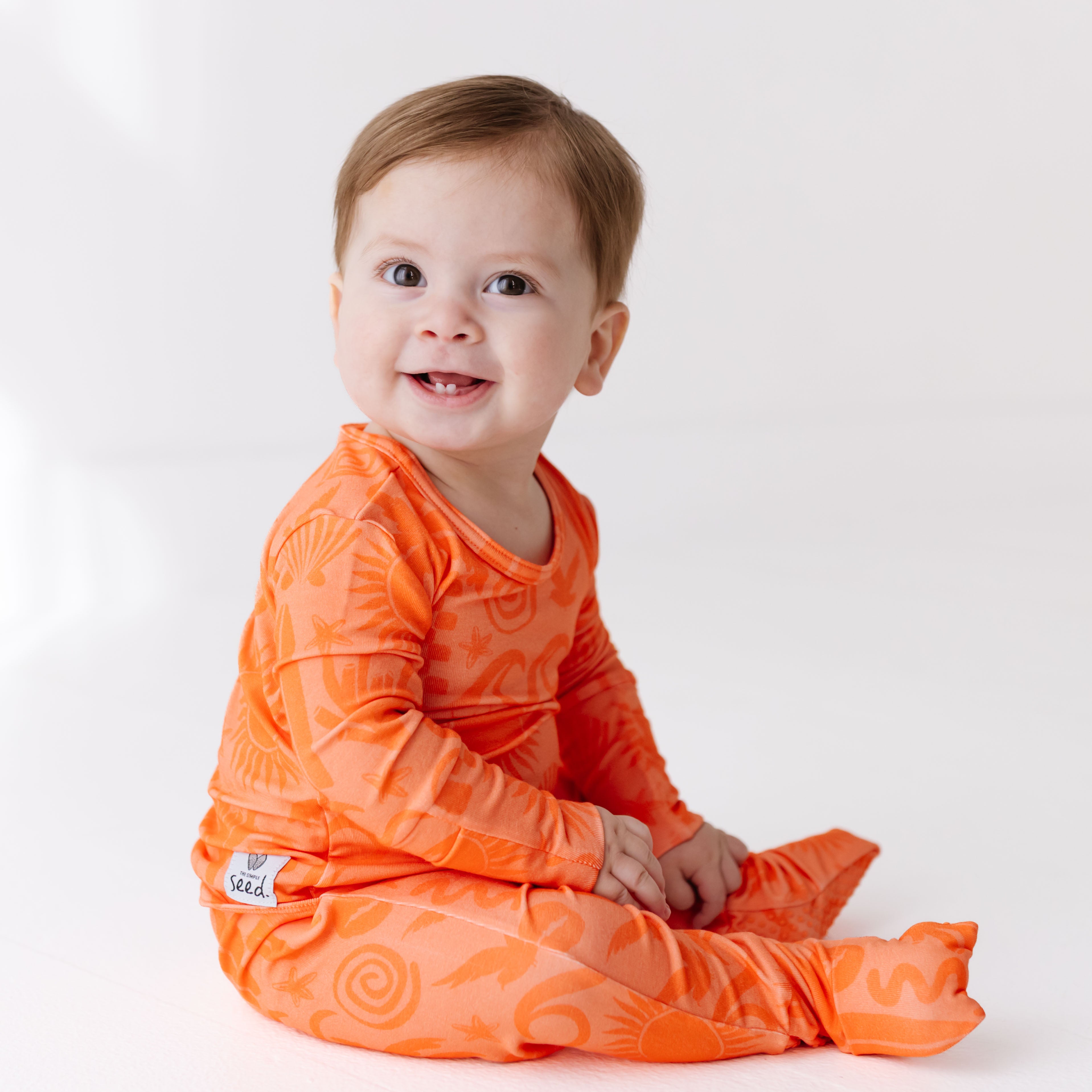 Baby wearing an orange onesie with a pattern on a white background