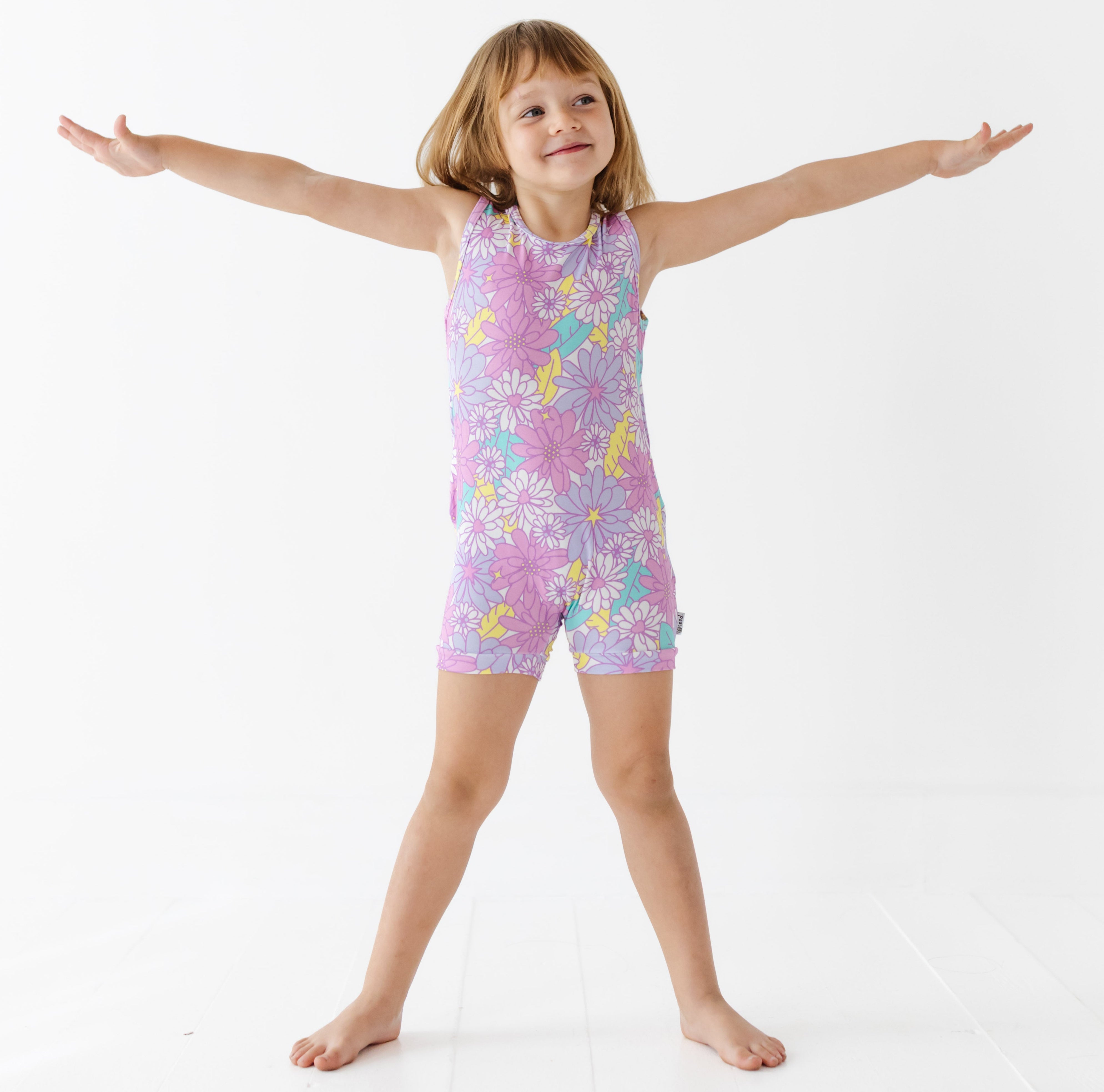 Child wearing a colorful floral romper with arms outstretched on a white background