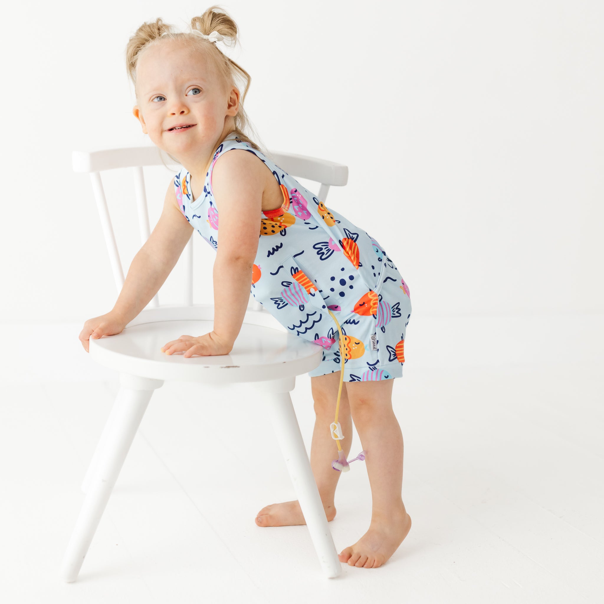 Child wearing a colorful dress with animal prints on a white chair.