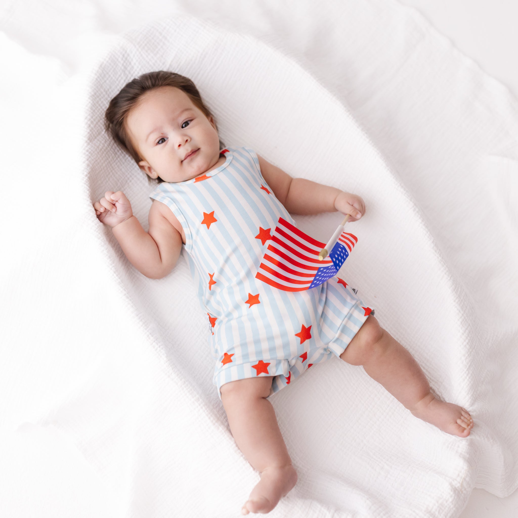Baby wearing a sleeveless top and shorts with American flag design on a white blanket