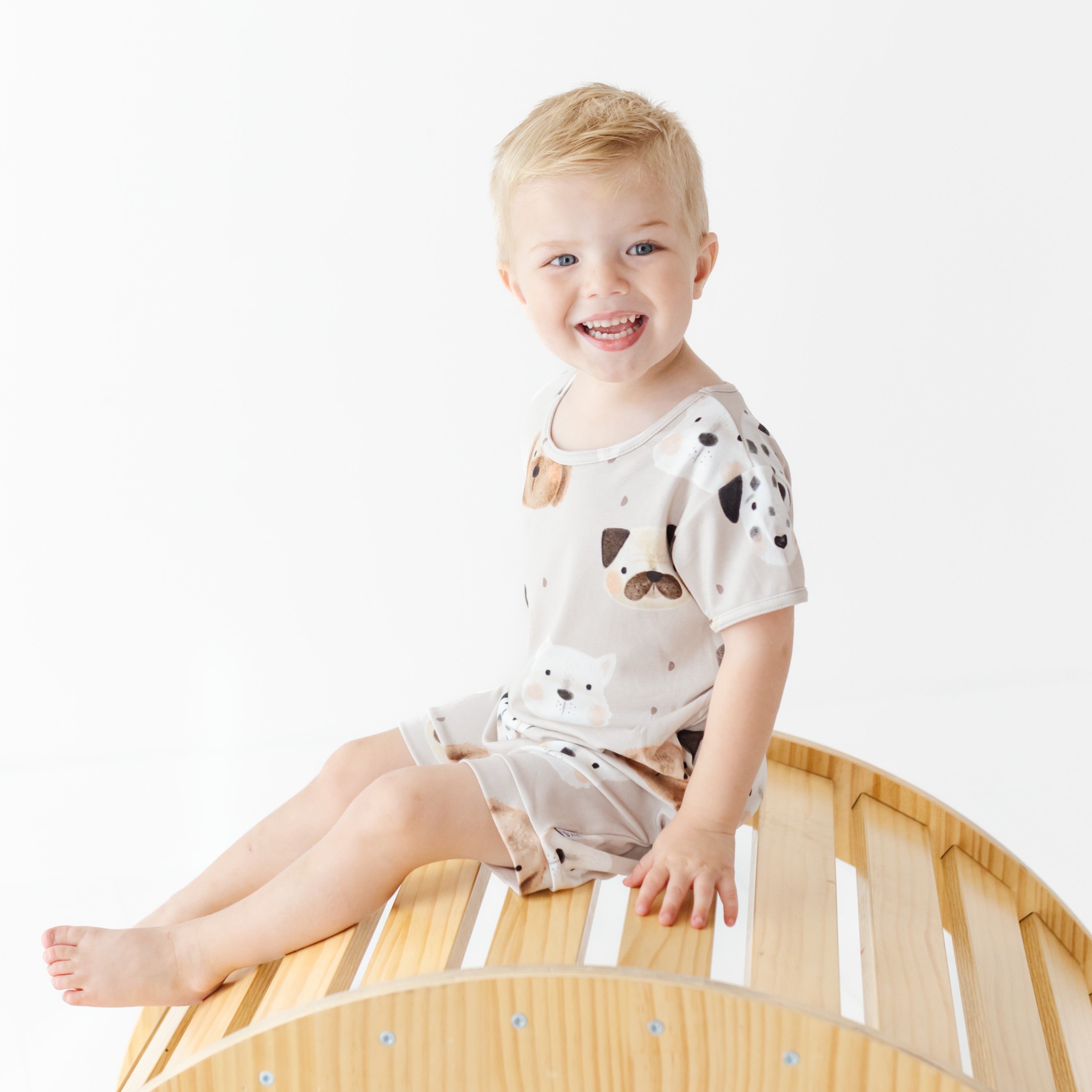 Child sitting on a wooden crib wearing a white outfit with black patterns.