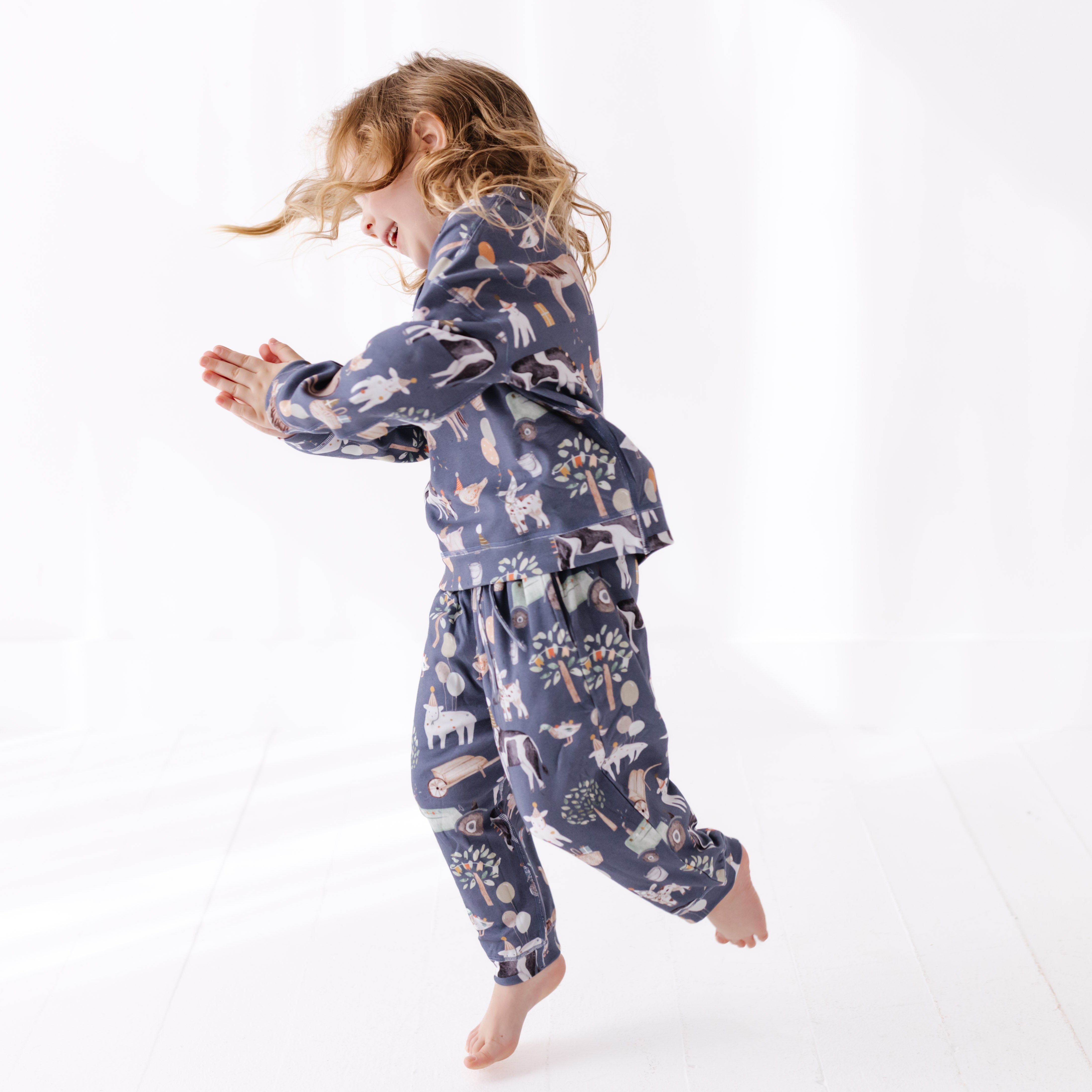 Child wearing a blue sweat set with party farm animal prints on a white background
