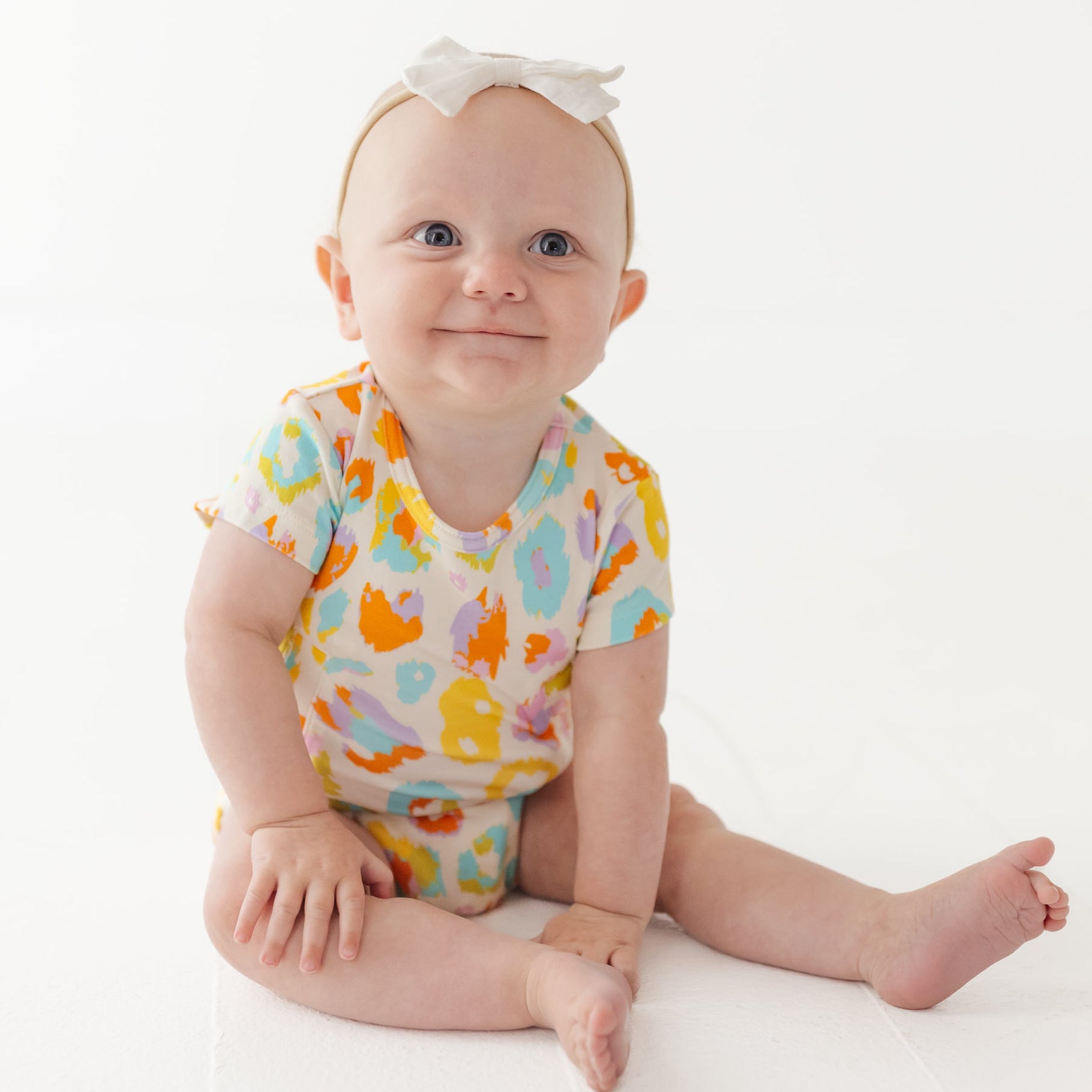 Baby wearing a colorful onesie with animal prints on a white background