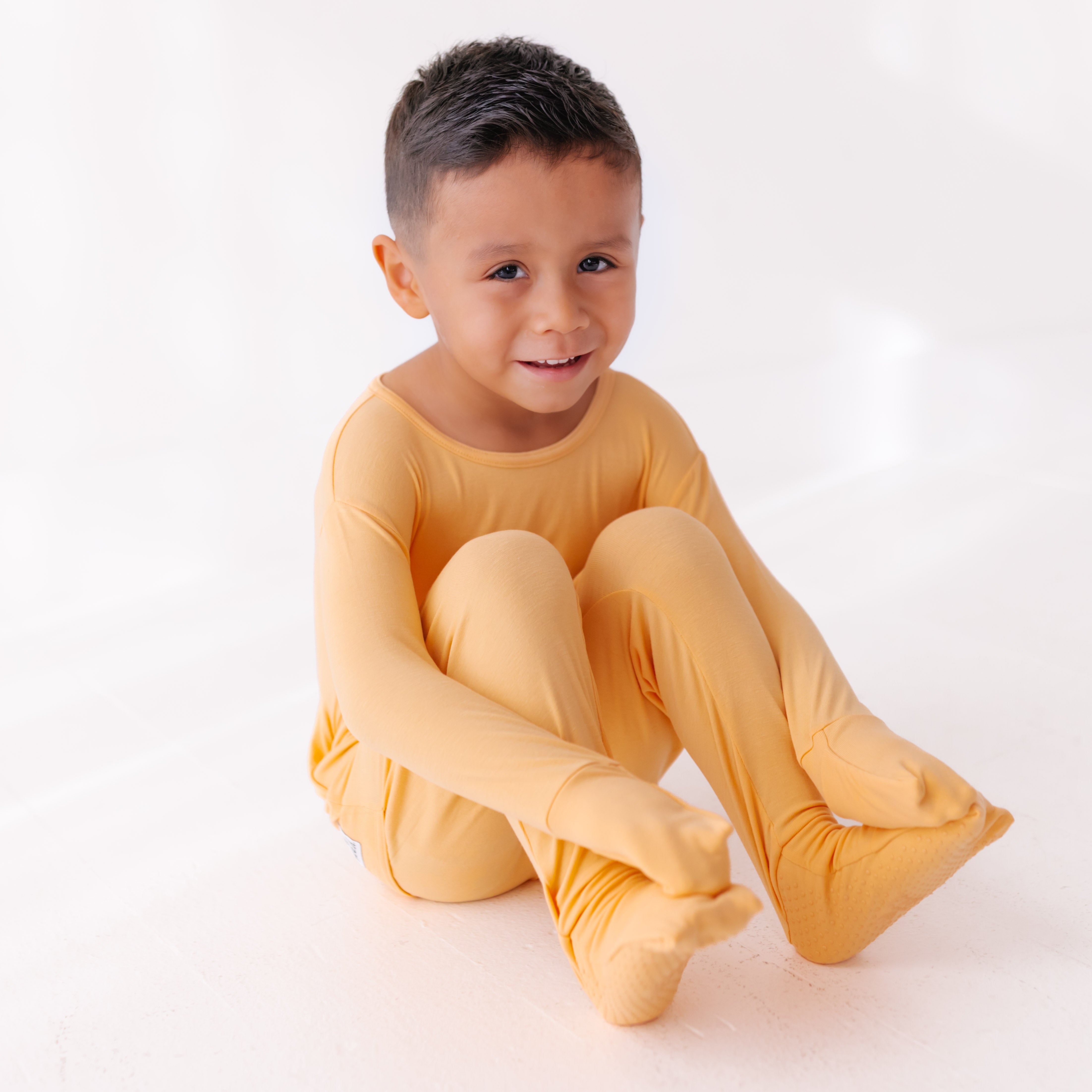 Child wearing a yellow outfit sitting on a white background