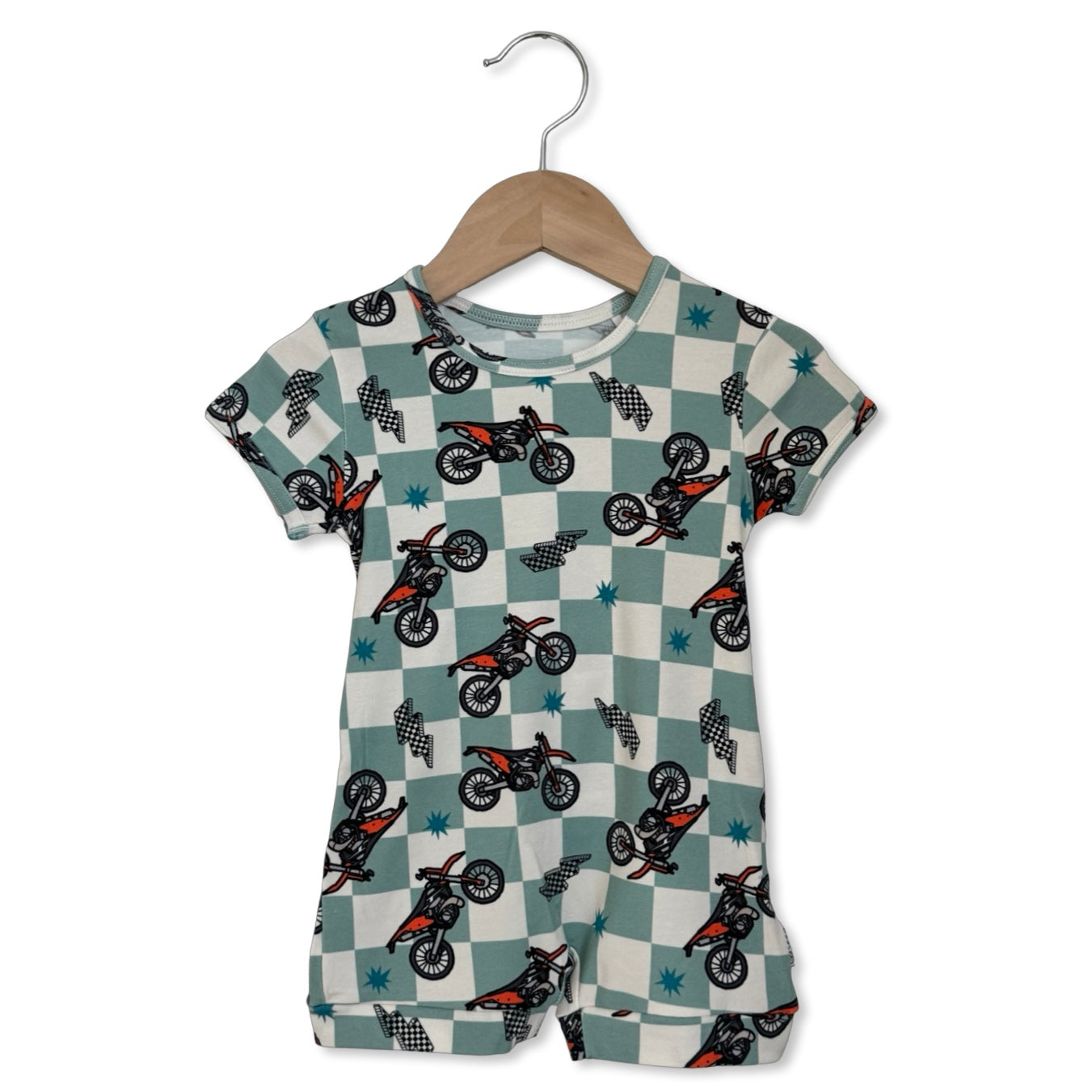Children's romper with dirt bike pattern on a checkered background, hanging on a wooden hanger.