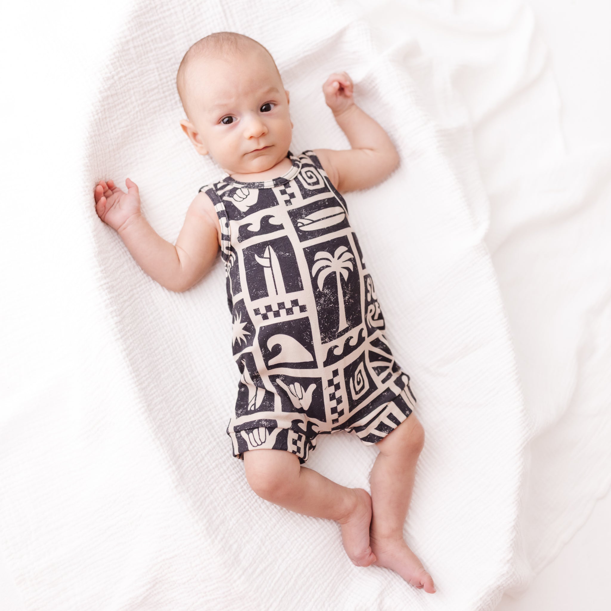 Baby wearing a black and white patterned romper on a white blanket
