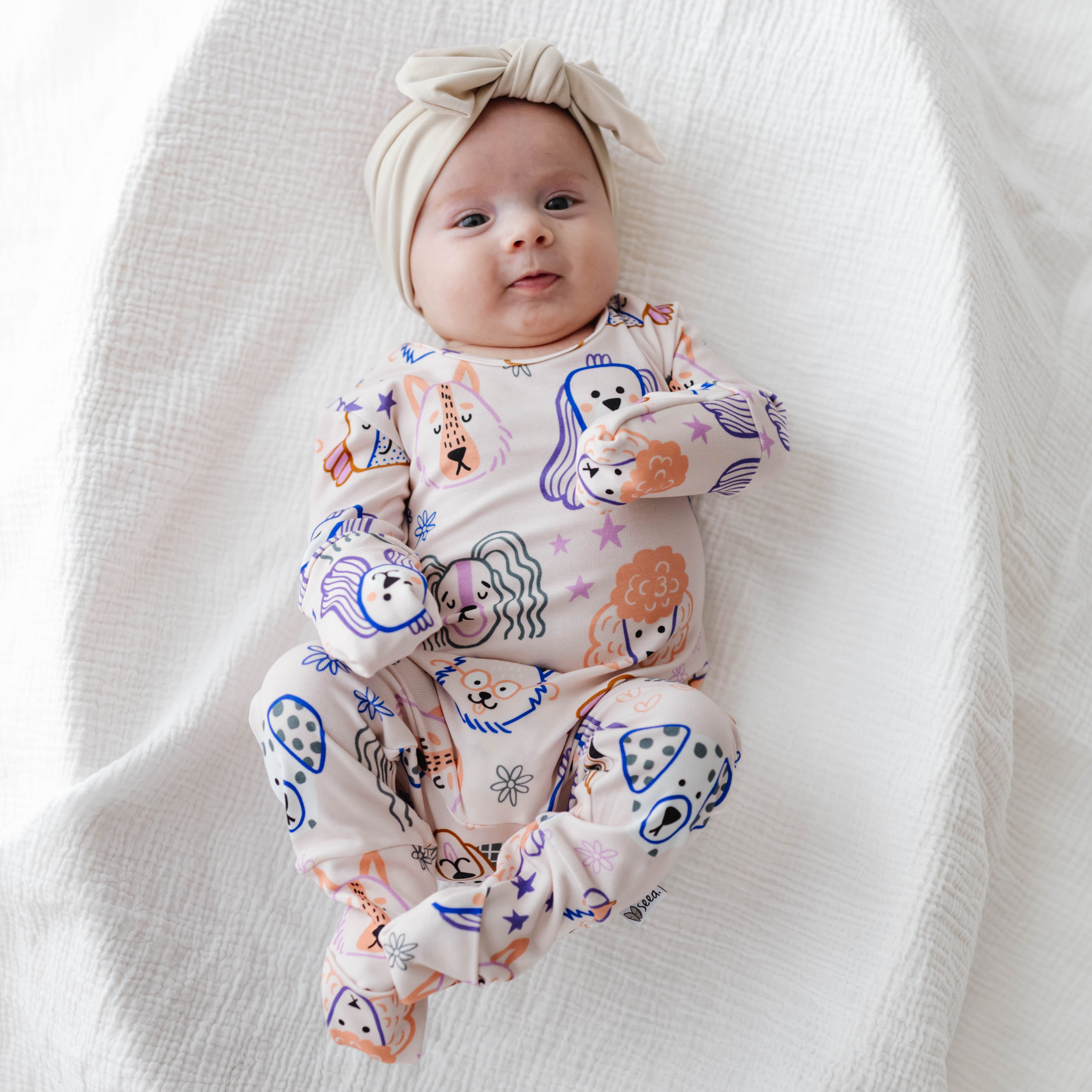Baby wearing a colorful onesie with animal prints on a white blanket