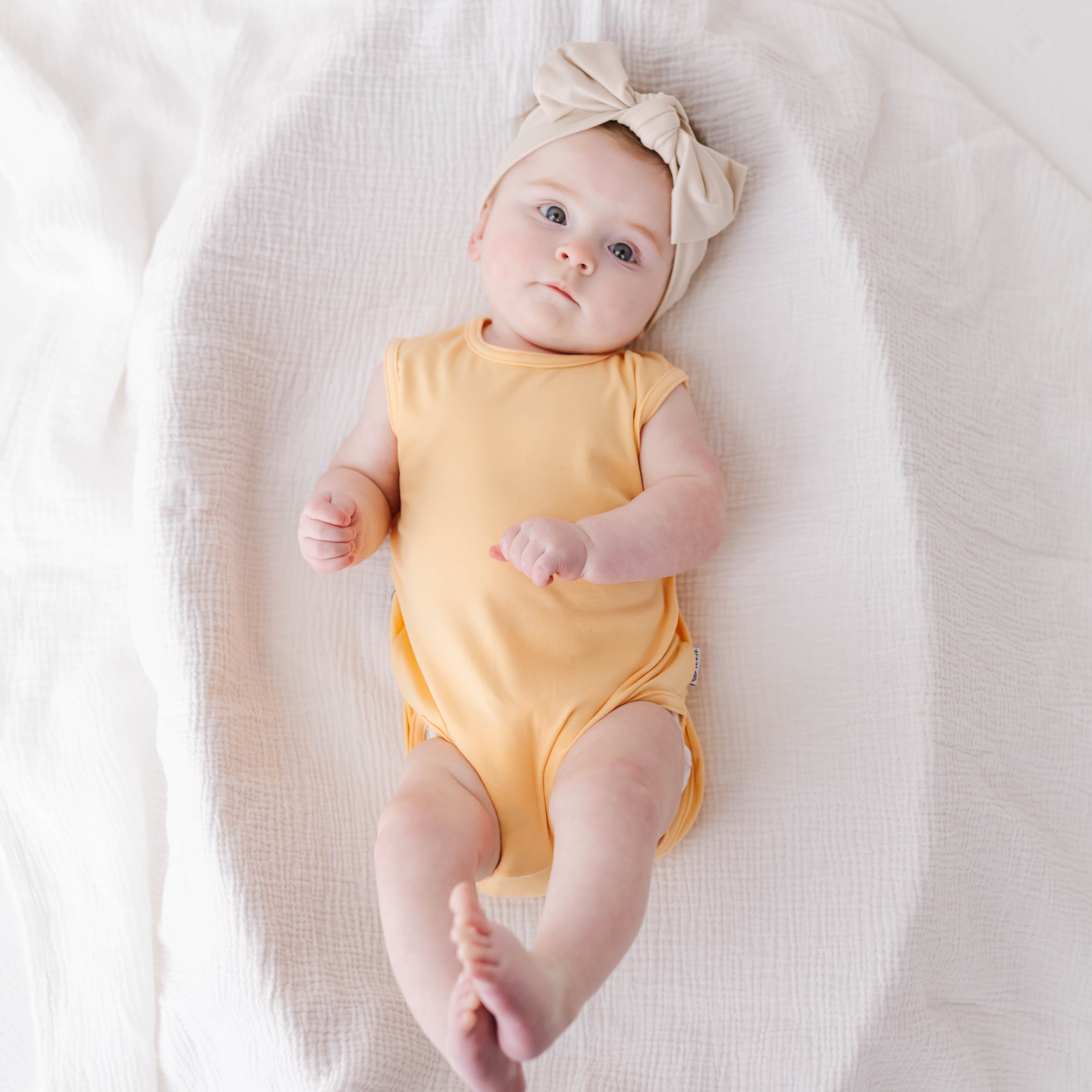 Baby in a yellow onesie and headband lying on a white blanket