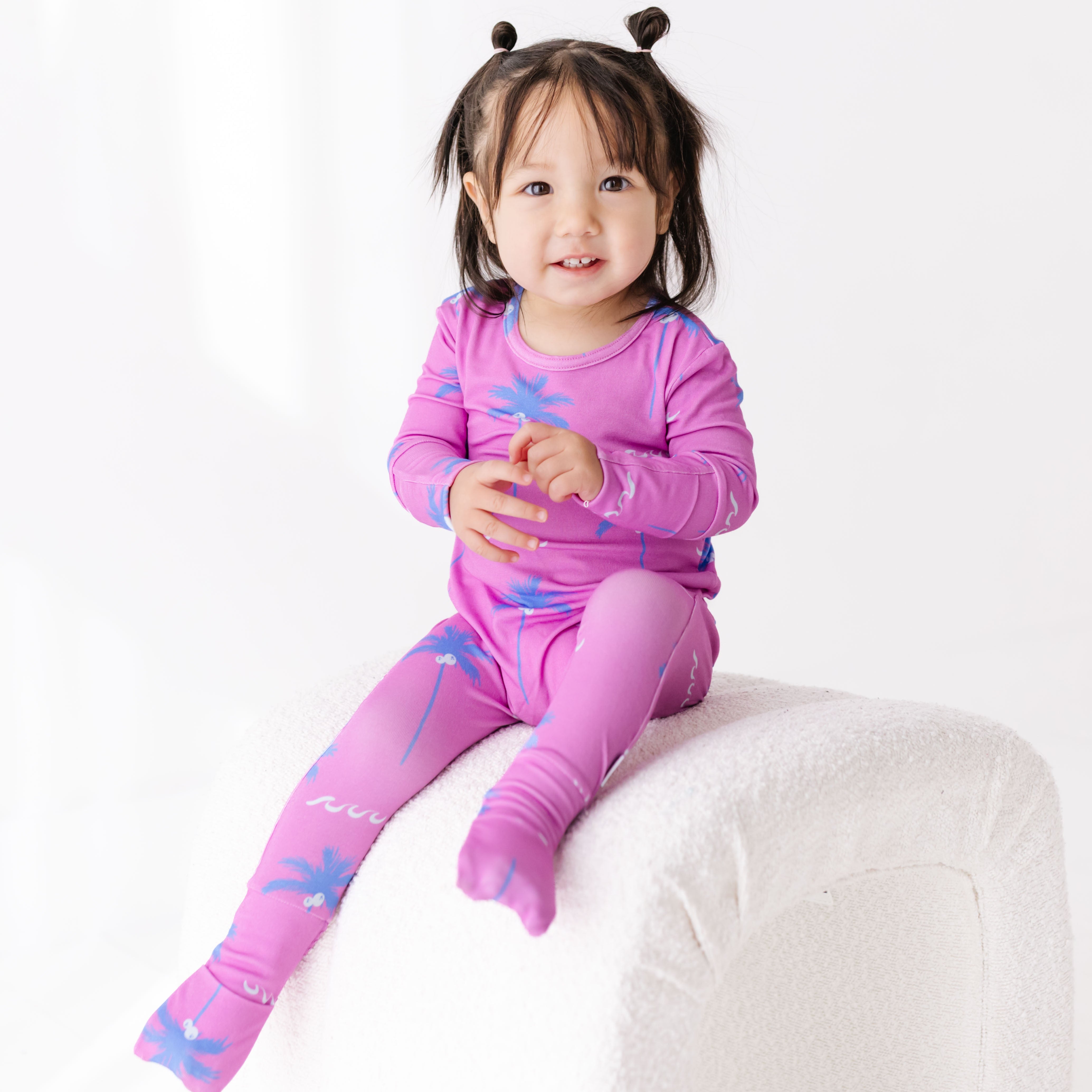 Child wearing a pink outfit with blue patterns sitting on a white surface.