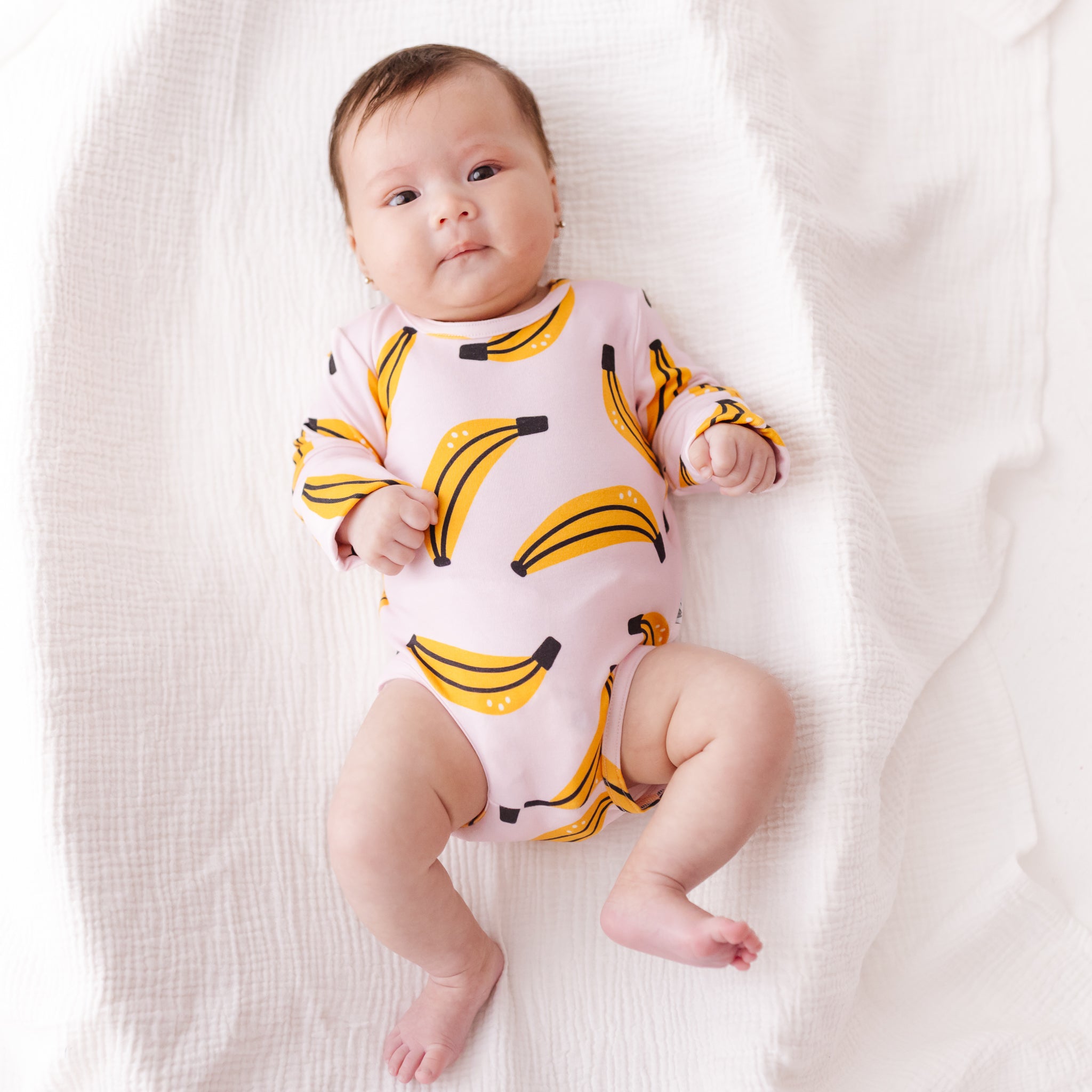 Baby wearing a pink onesie with banana pattern on a white blanket