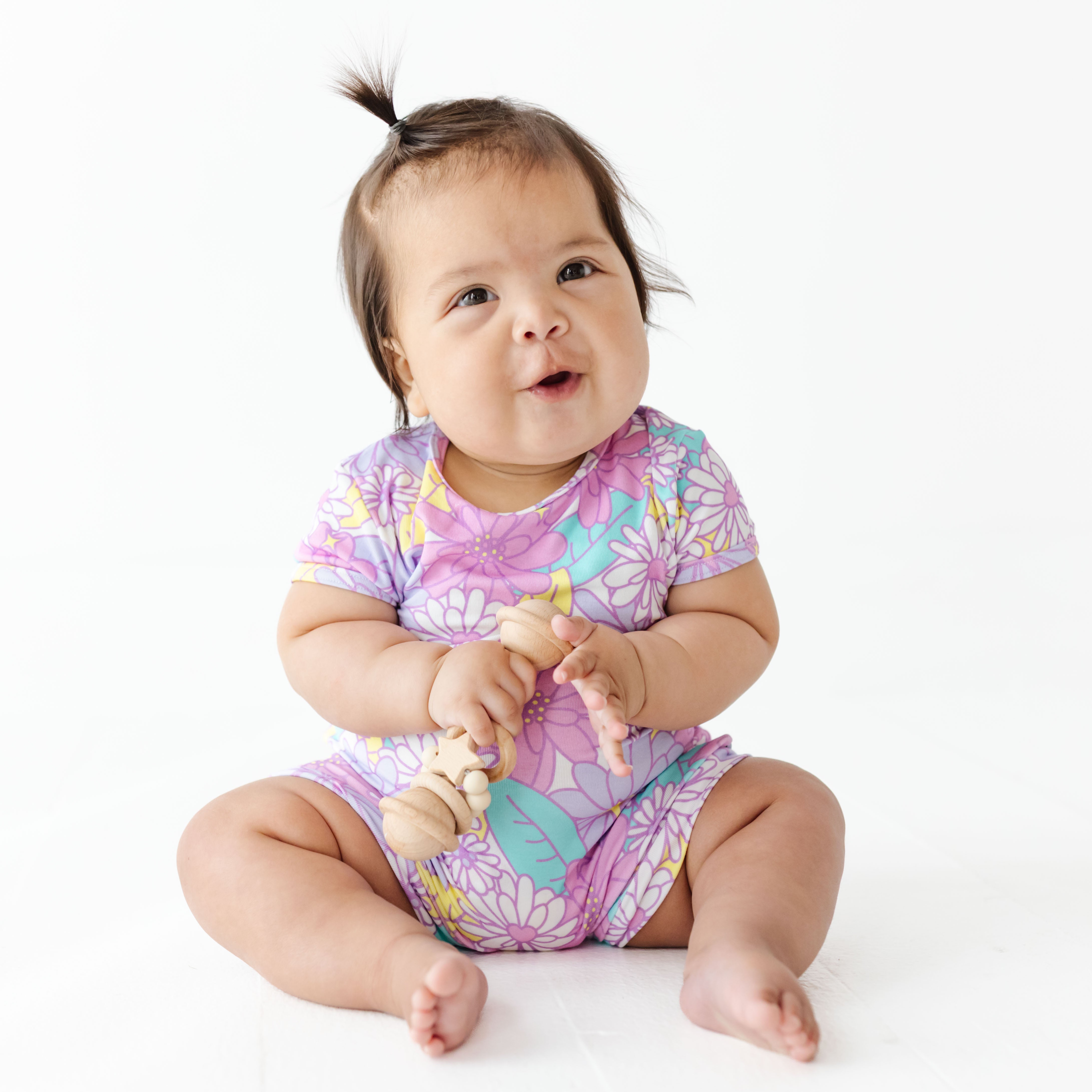 Baby wearing a colorful floral onesie sitting on a white background