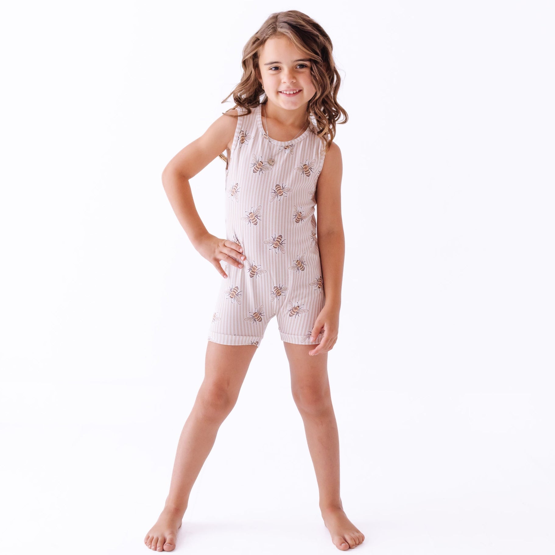 Girl wearing sleeveless romper with stripes and bees on a white background 