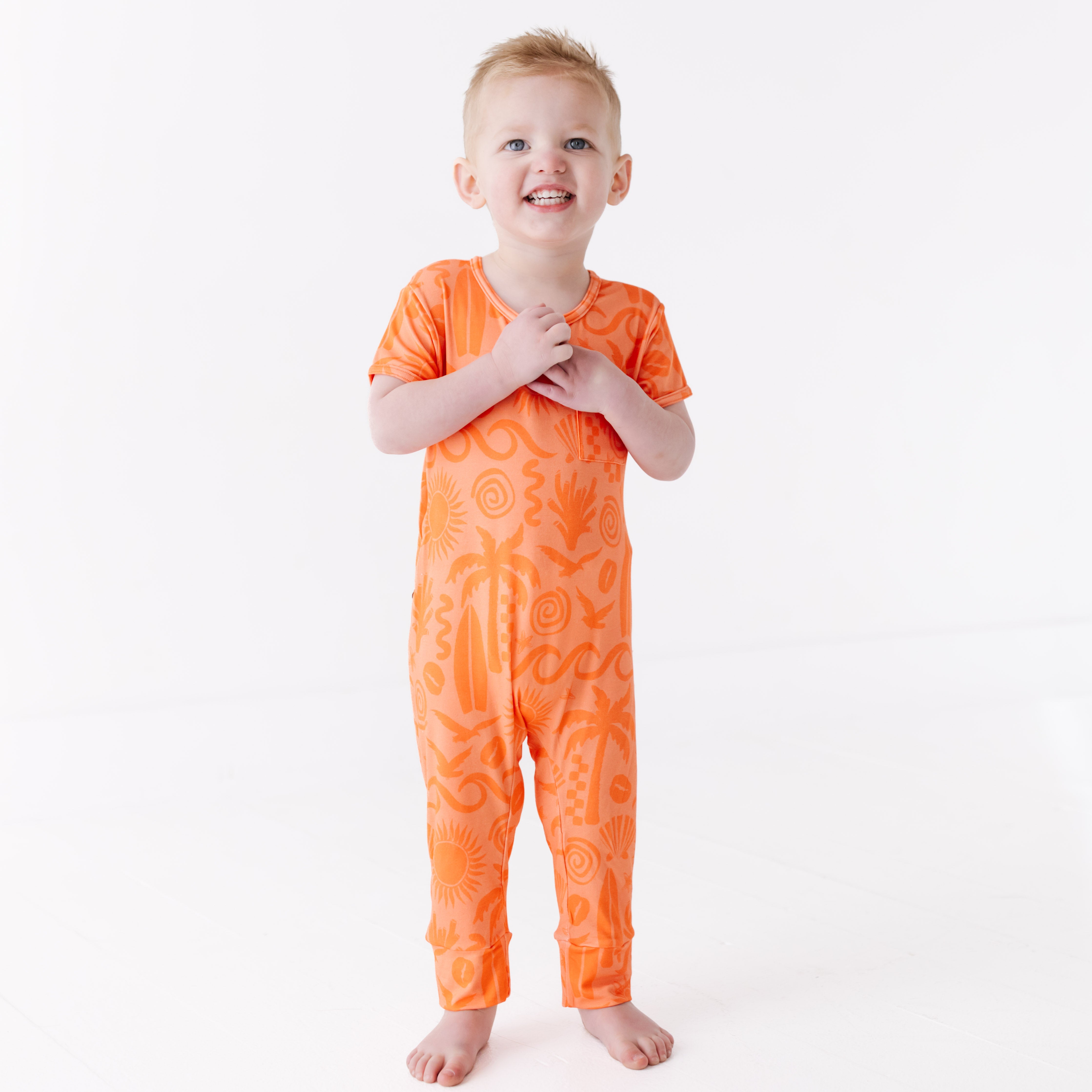 Child wearing an orange patterned onesie on a white background