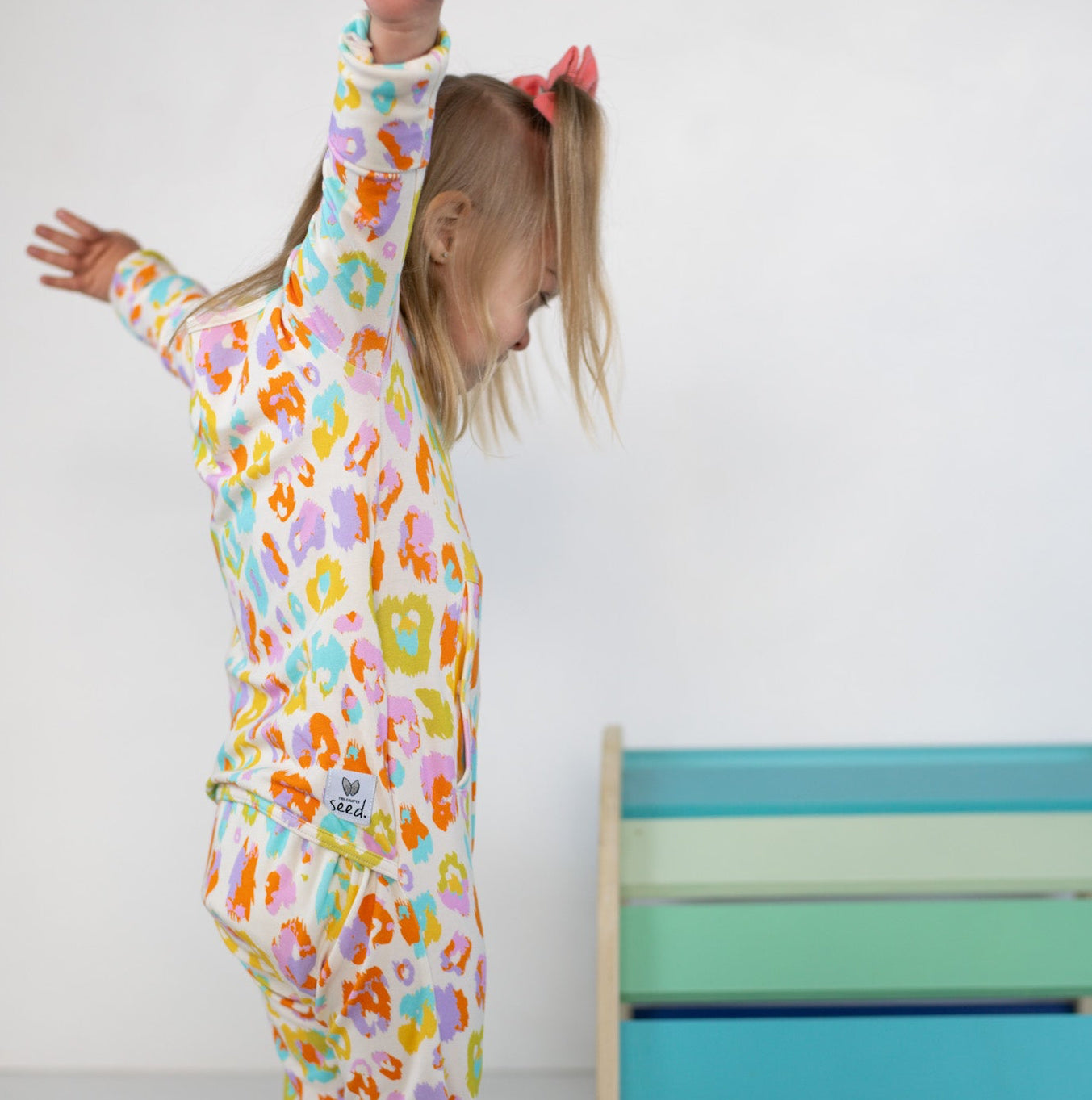 Child wearing colorful pajamas with a pattern of animals, standing in a room with a bed in the background.