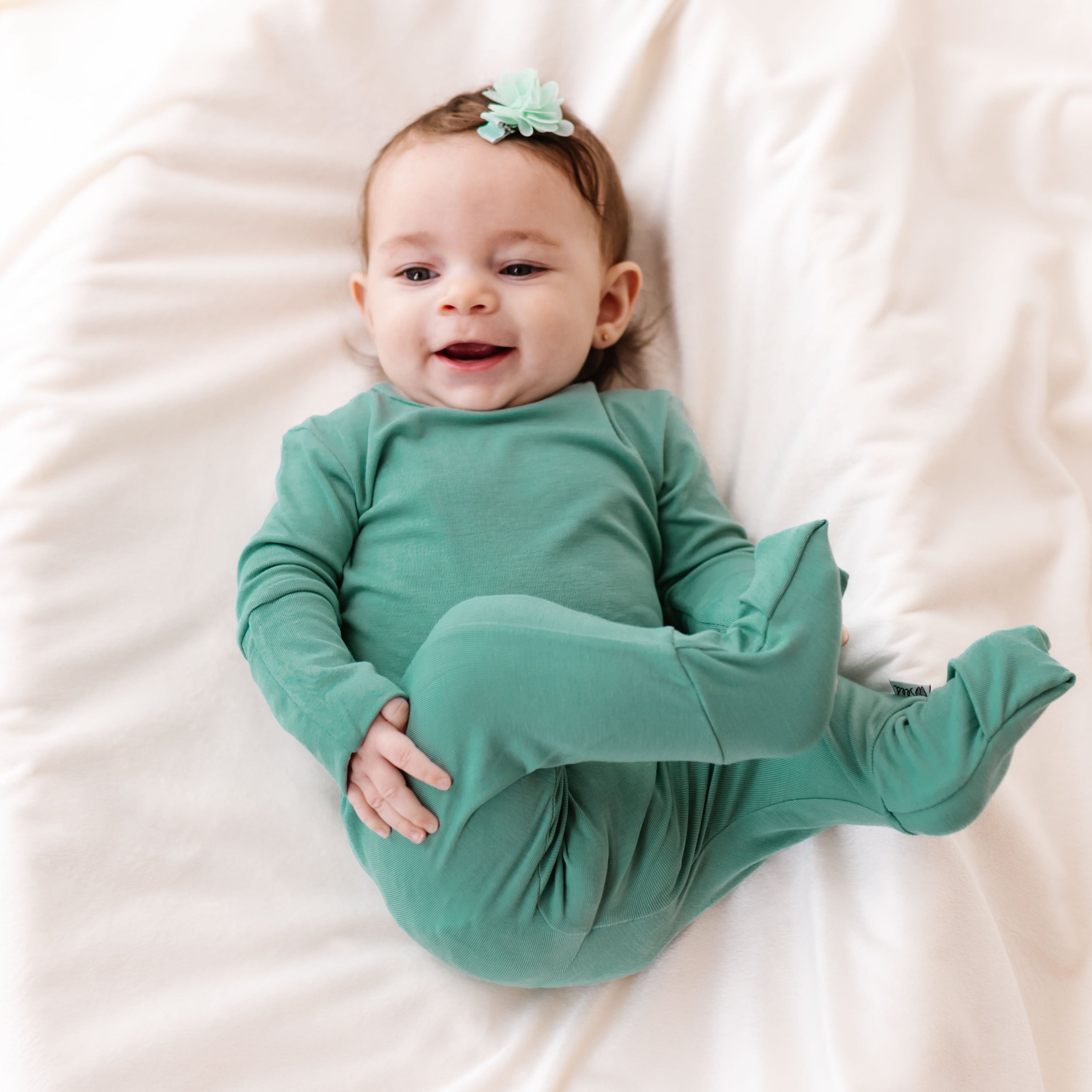 Baby in a green onesie lying on a white blanket