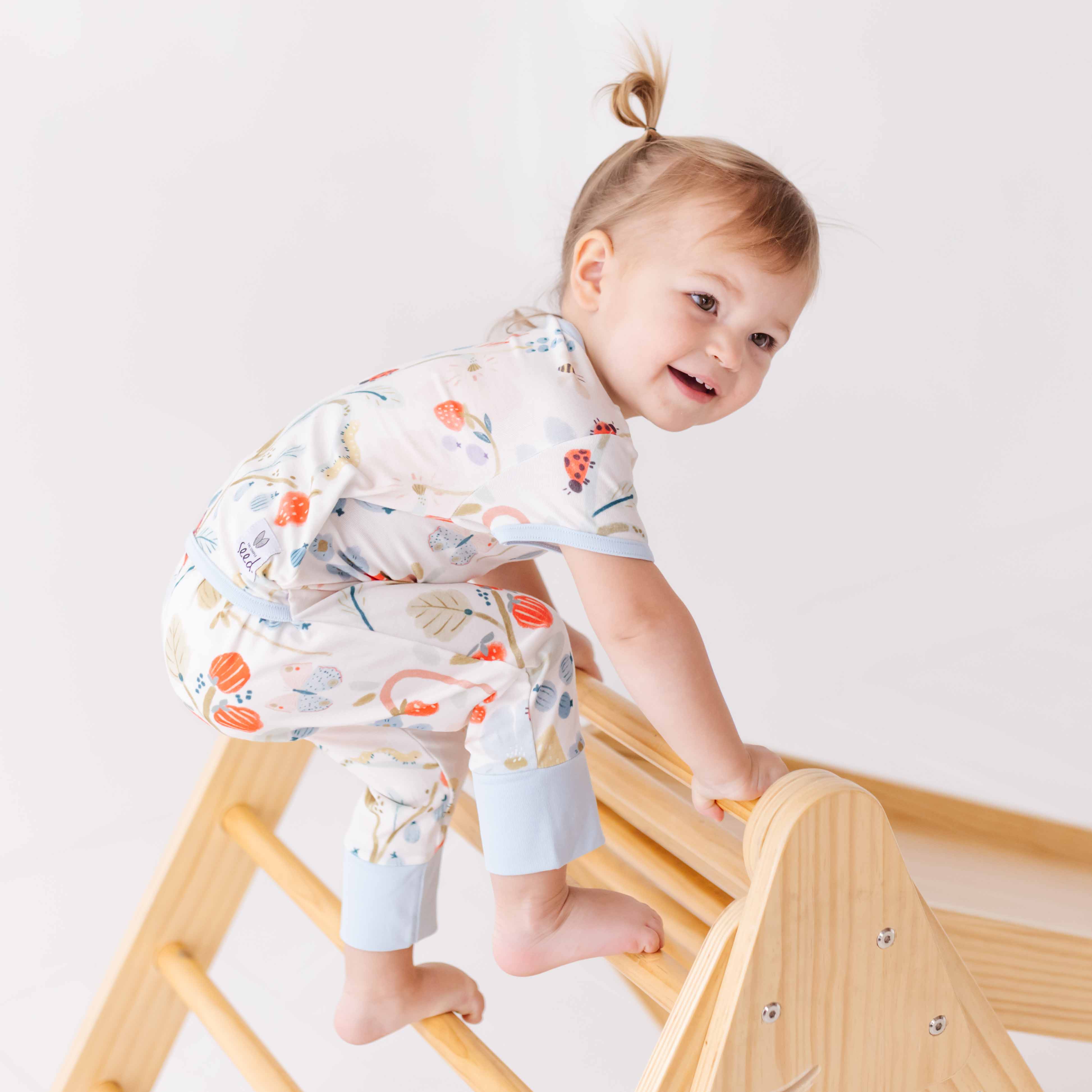 Baby in a floral outfit climbing a wooden梯子