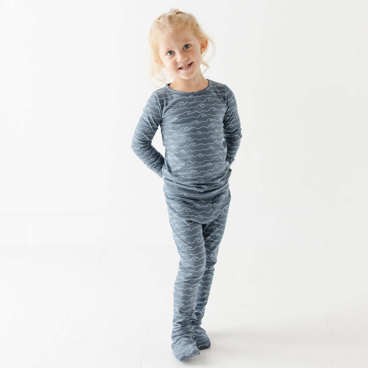 A girl stand on white floors wearing blue pajama set with waves on it. 