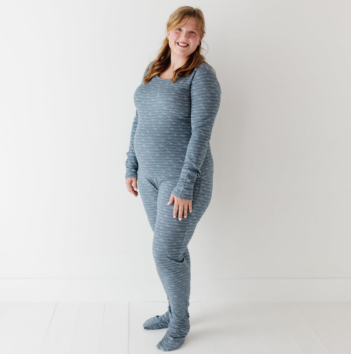 A smiling woman stands on white floor wearing blue romper with waves on it. 