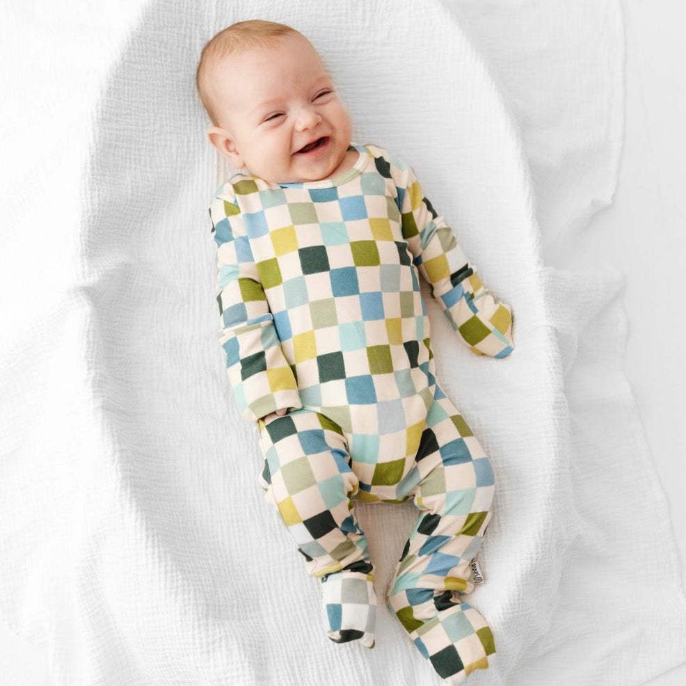 Baby wearing a colorful checkered onesie lying on a white blanket