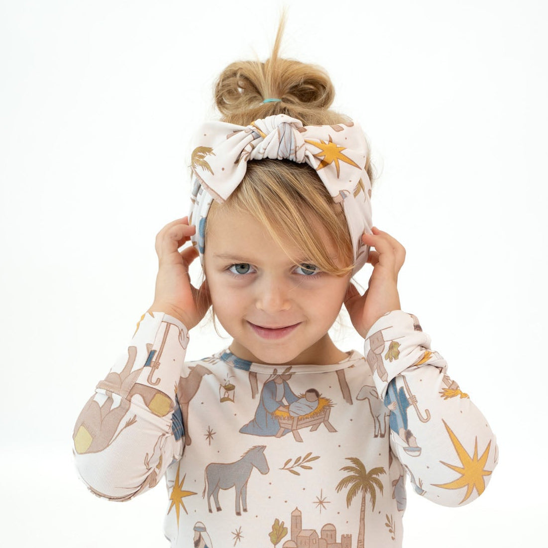 A young child wearing a matching long-sleeve pajama set with an animal and desert-themed print, sitting in a split position against a bright white background.