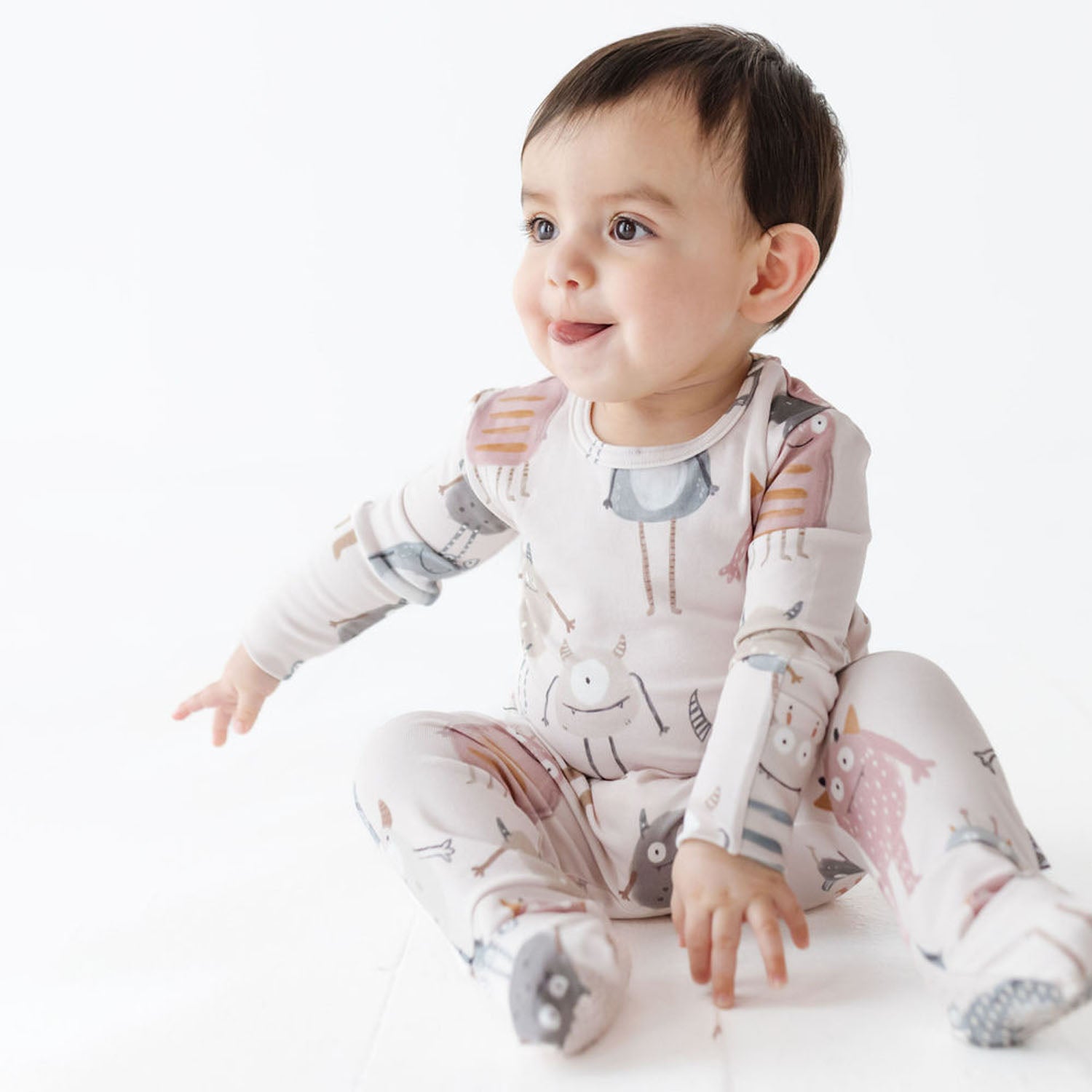 Baby wearing a patterned onesie sitting on a white surface