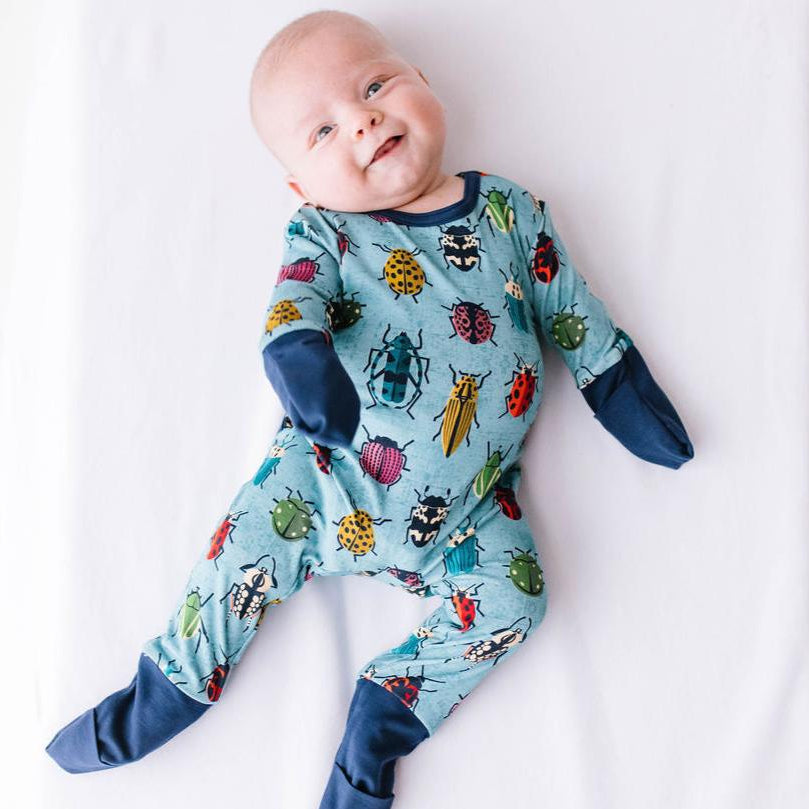 A smiling baby lying down wearing a long-sleeved romper with a colorful buggy pattern and fold-over footies.