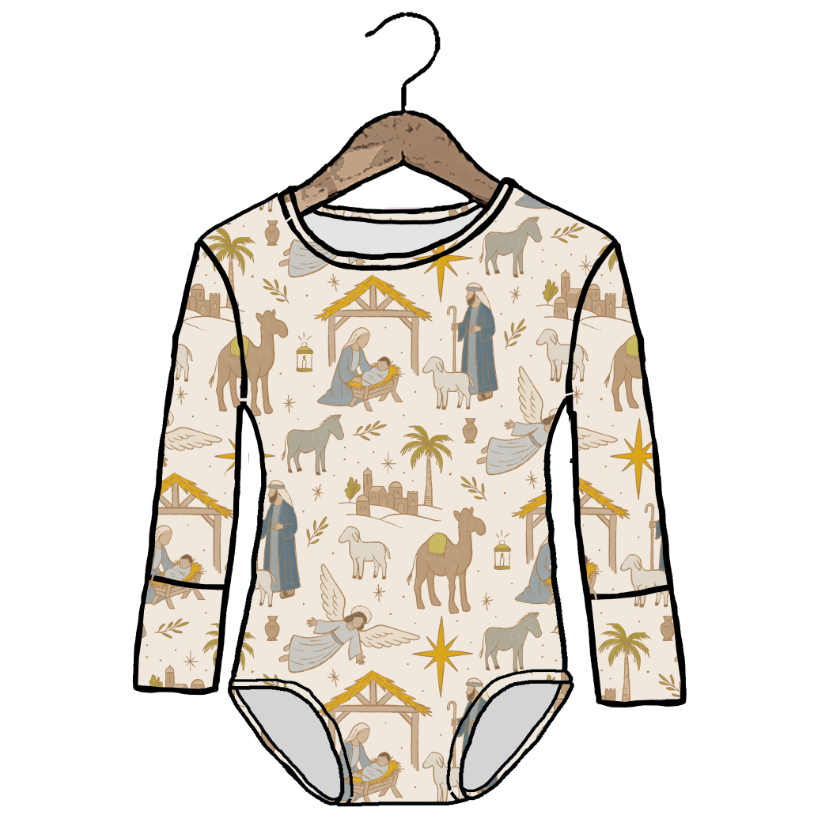 A long-sleeve baby bodysuit with an all-over Christmas nativity print, shown on a wooden hanger against a plain white background. The bodysuit features illustrations of camels, angels, shepherds, and a stable on an off-white base.