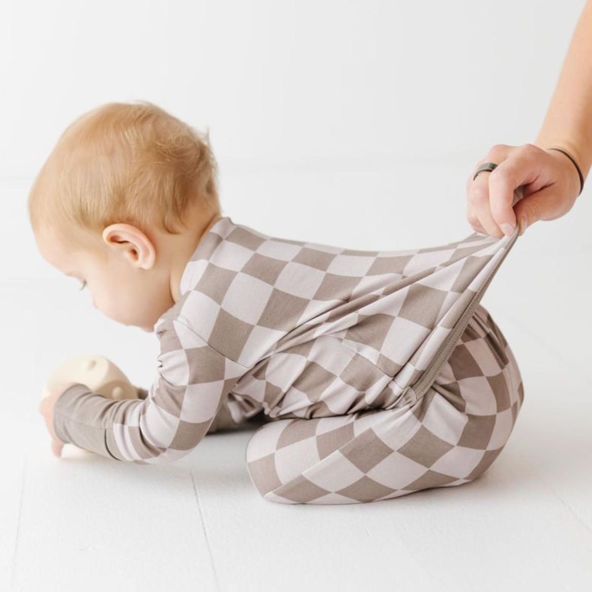 Baby in a checkered outfit being held by an adult on a white background