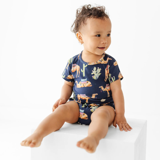 Baby wearing a navy blue onesie with animal prints on a white background
