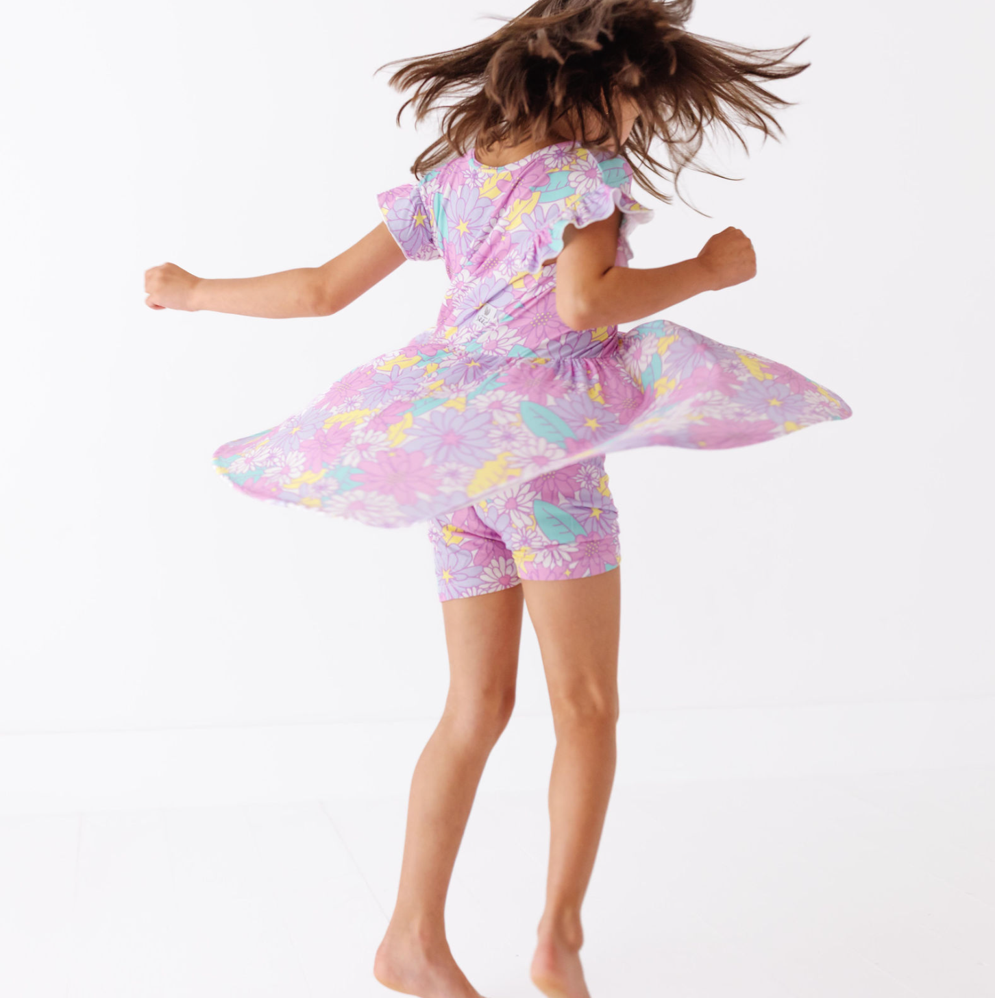 Child wearing a pink floral dress with ruffled sleeves and shorts on a white background