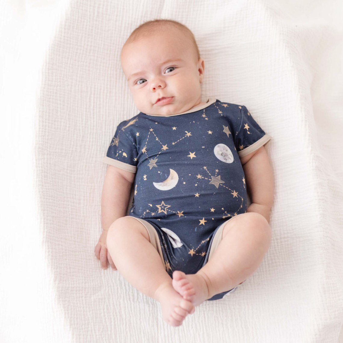 Baby wearing a navy blue onesie with celestial pattern on a white blanket