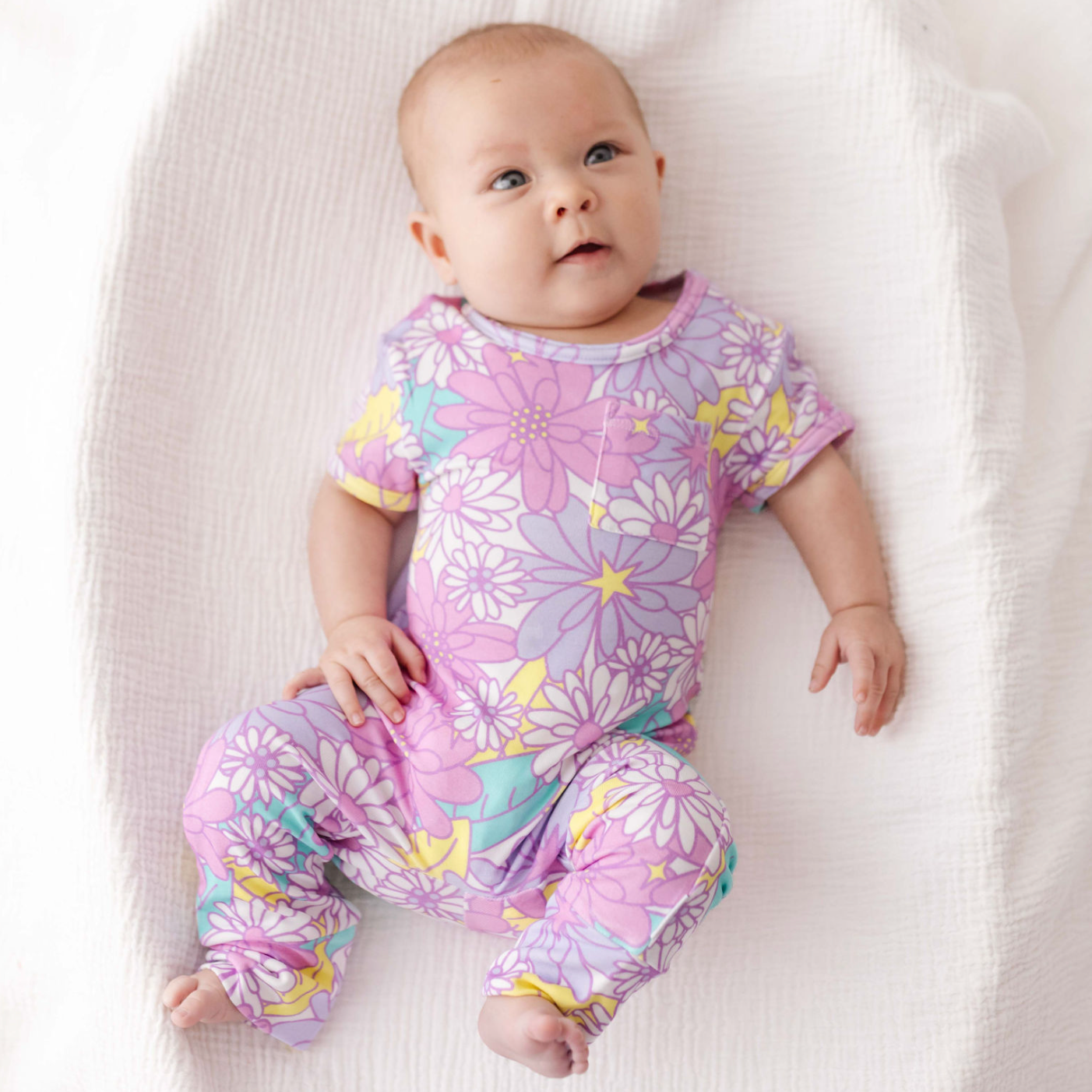 Baby wearing a purple floral onesie on a white blanket
