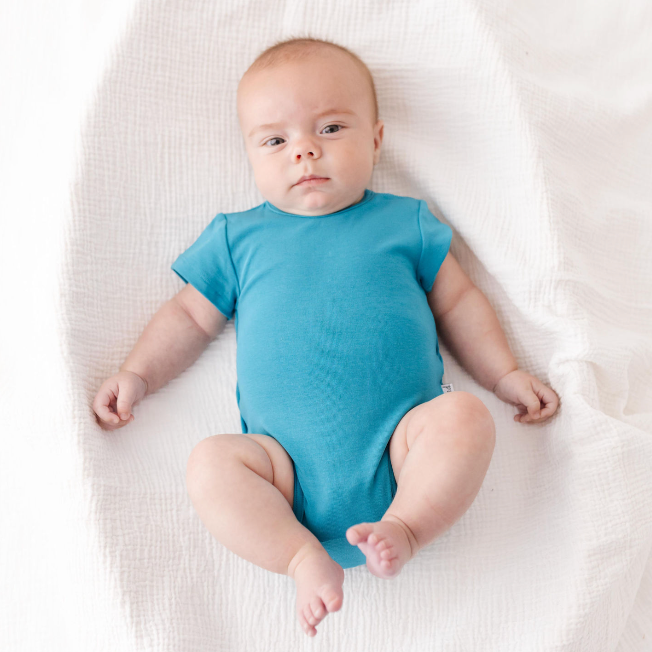 Baby wearing a blue onesie lying on a white blanket