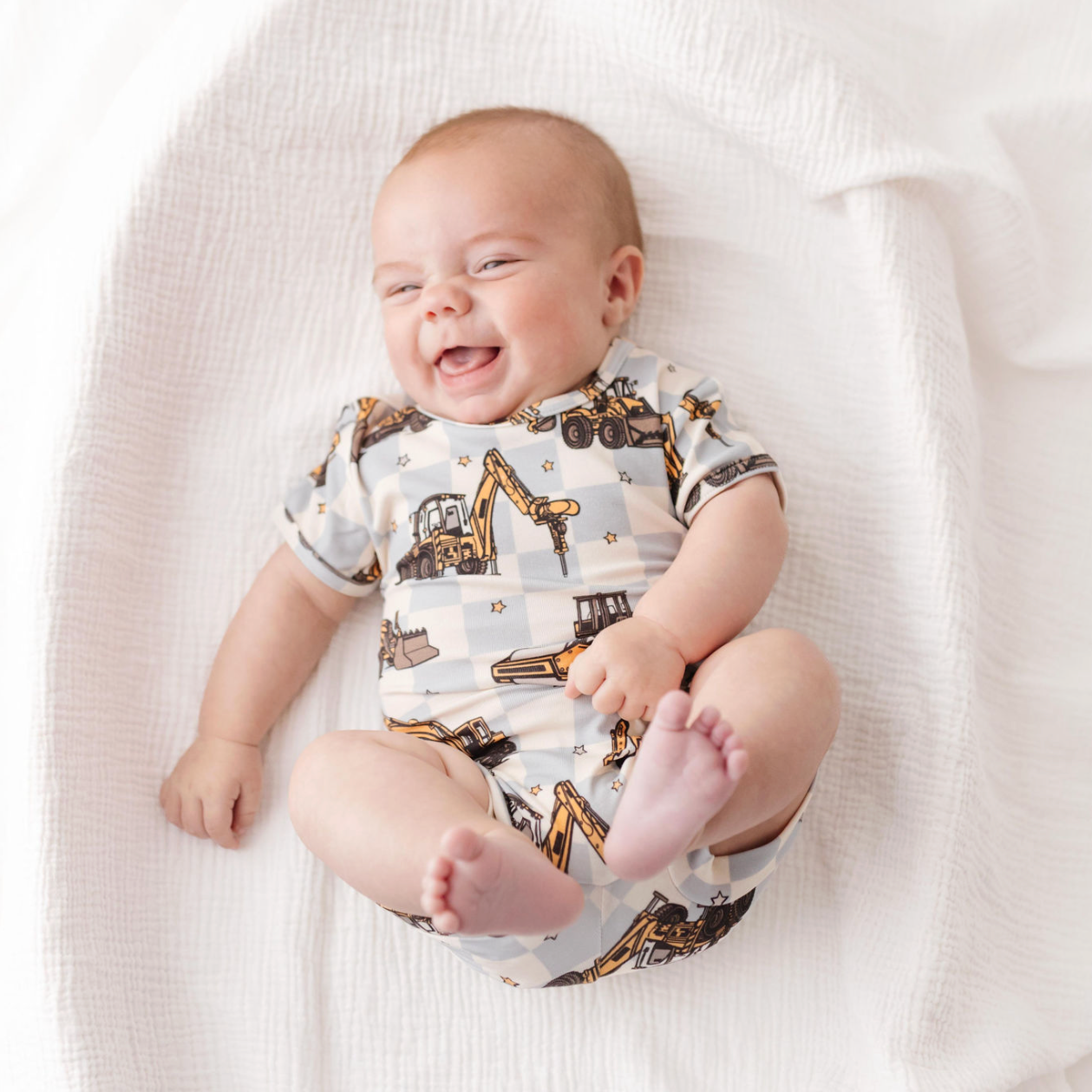 Baby wearing a onesie with construction vehicle pattern on a white blanket