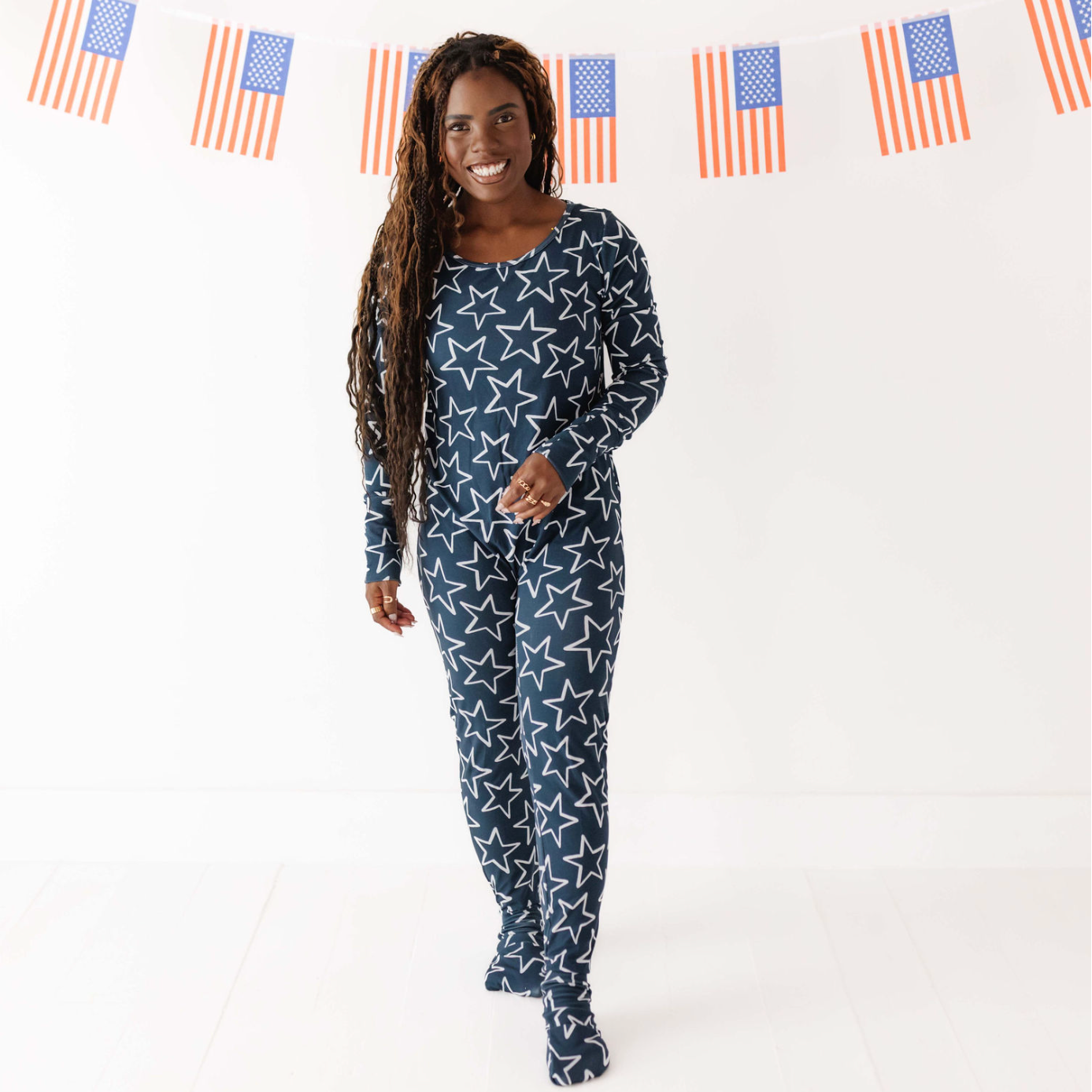 Woman wearing a navy blue pajama set with white star pattern in front of American flags.