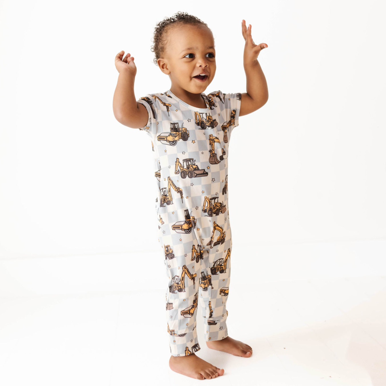 Baby wearing a onesie with construction vehicle pattern on a white background