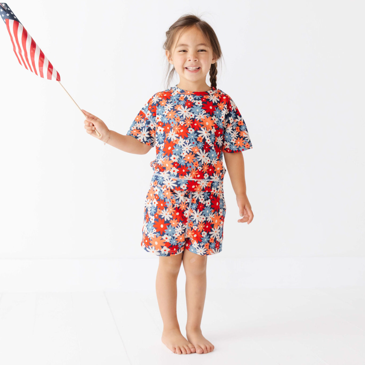 Child wearing a floral dress holding an American flag on a white background