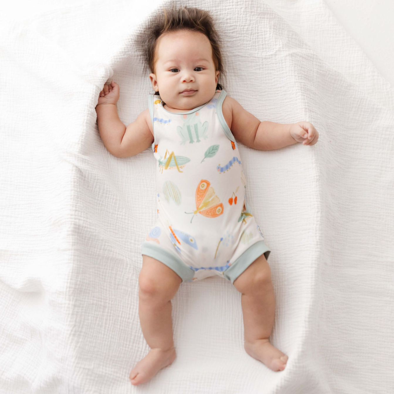 Baby lying on a white blanket wearing a colorful onesie.