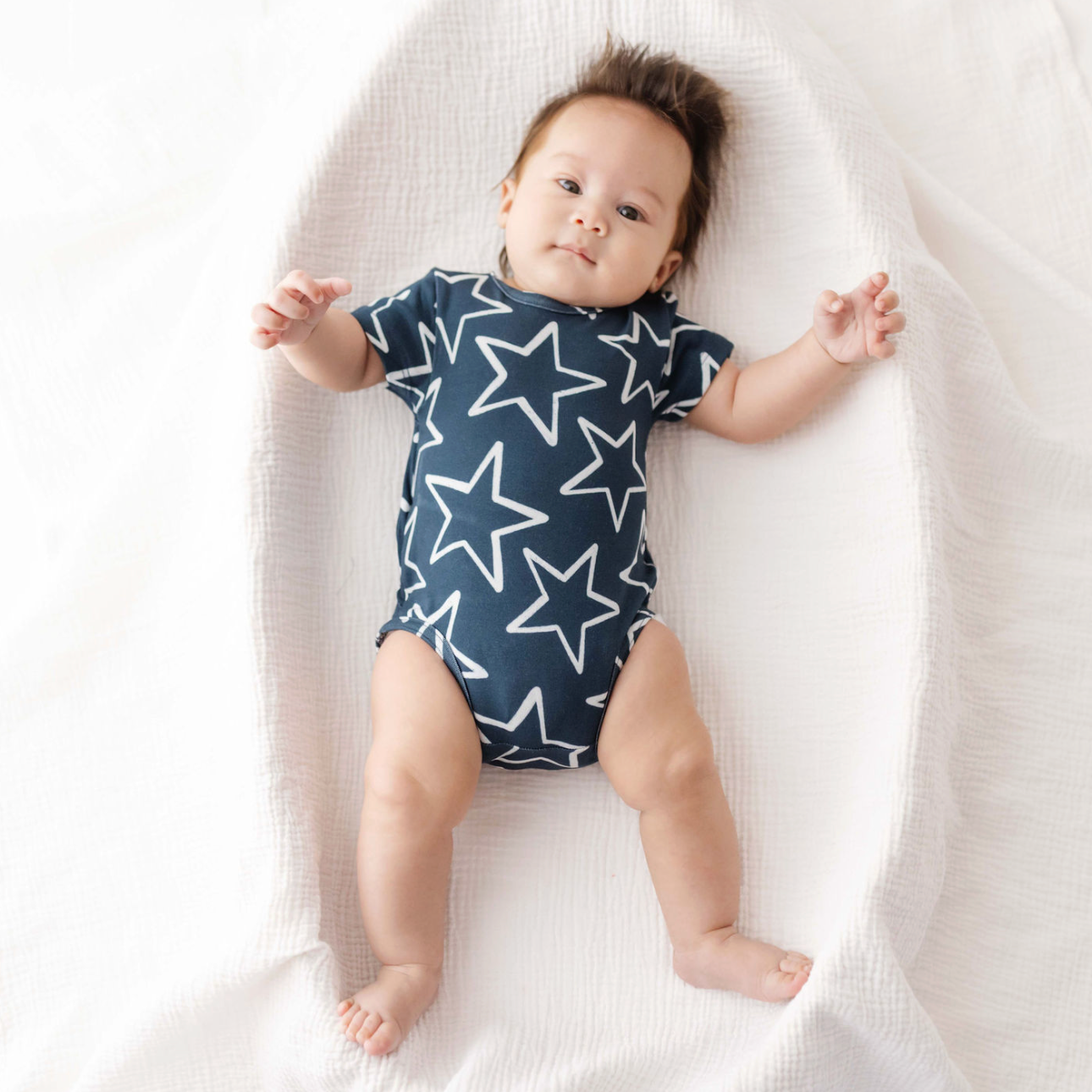 Baby wearing a navy blue onesie with white star patterns, lying on a white blanket.
